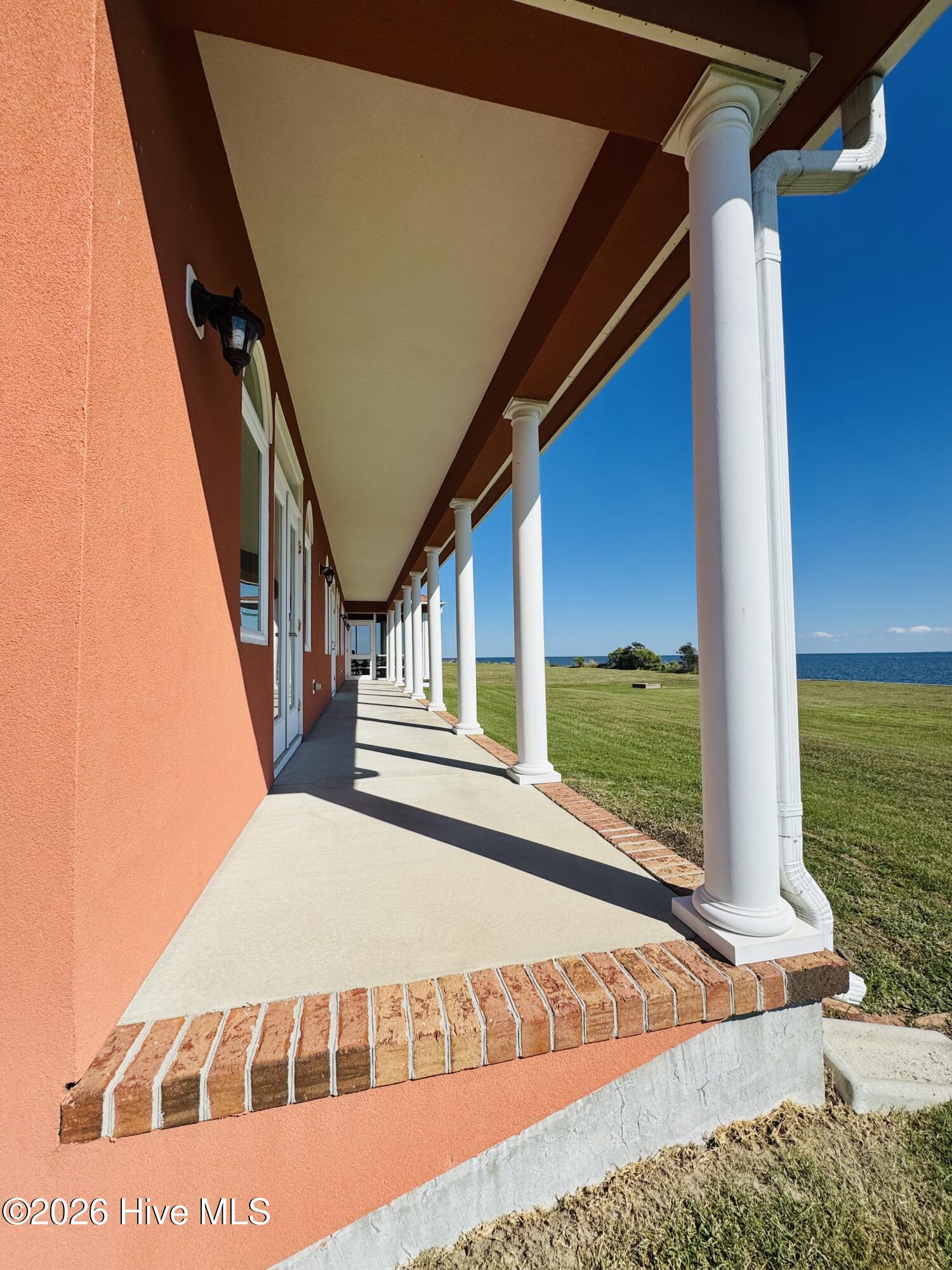 Covered porch with white columns beside a lawn overlooking blue water.