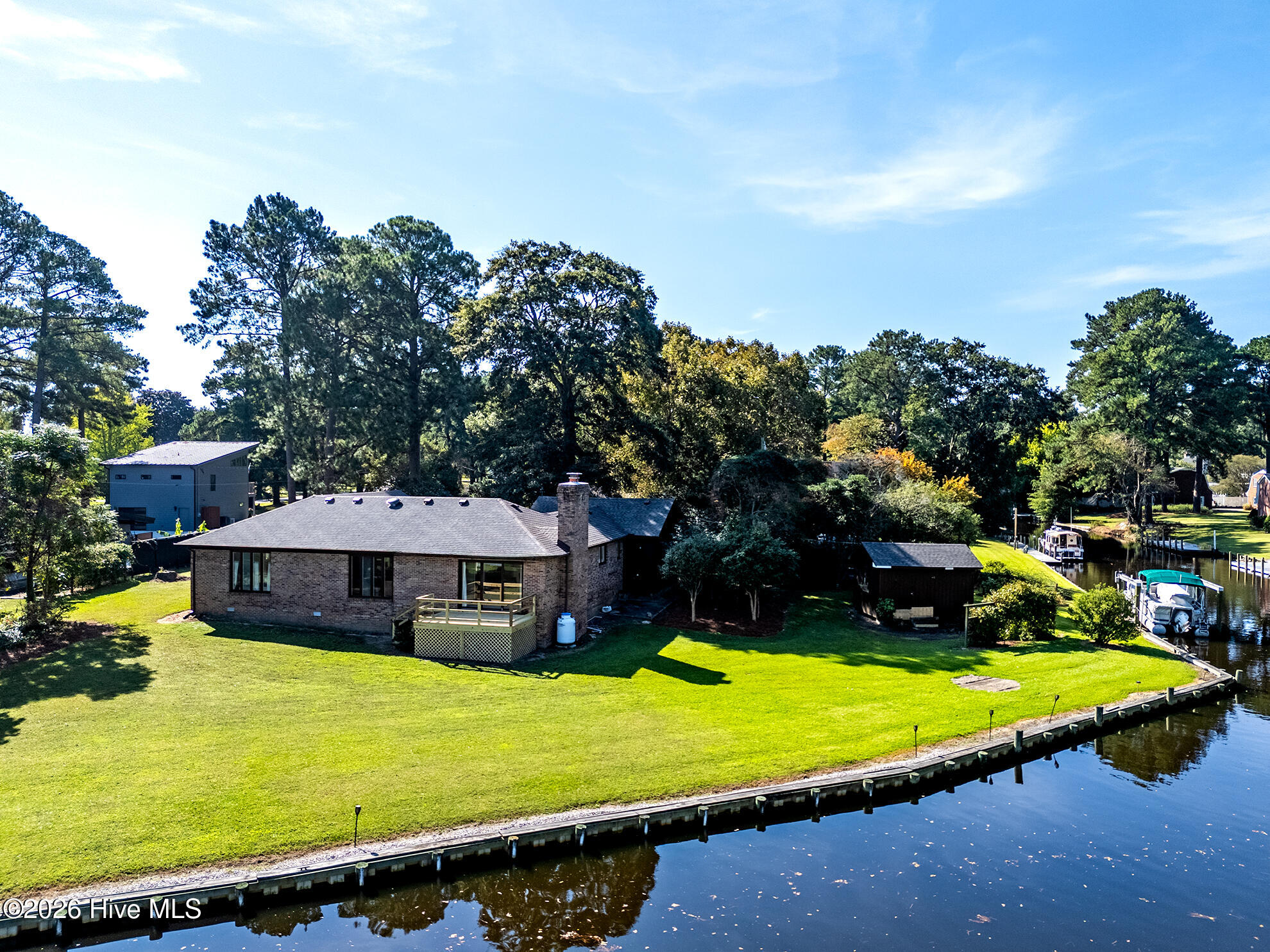Aerial view of a brick waterfront home beside a canal and shoreline bulkhead.