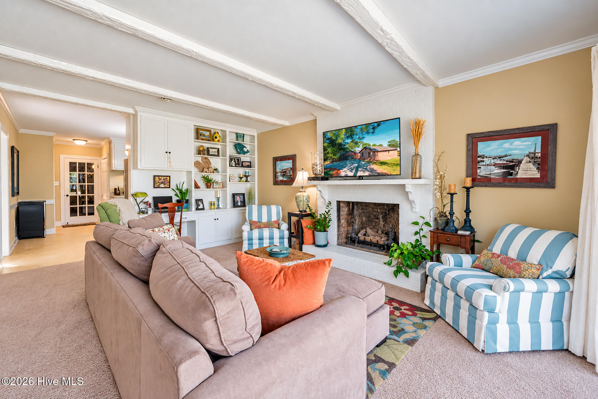 Furnished living room with exposed beams, built-in shelves, and a white brick fireplace.