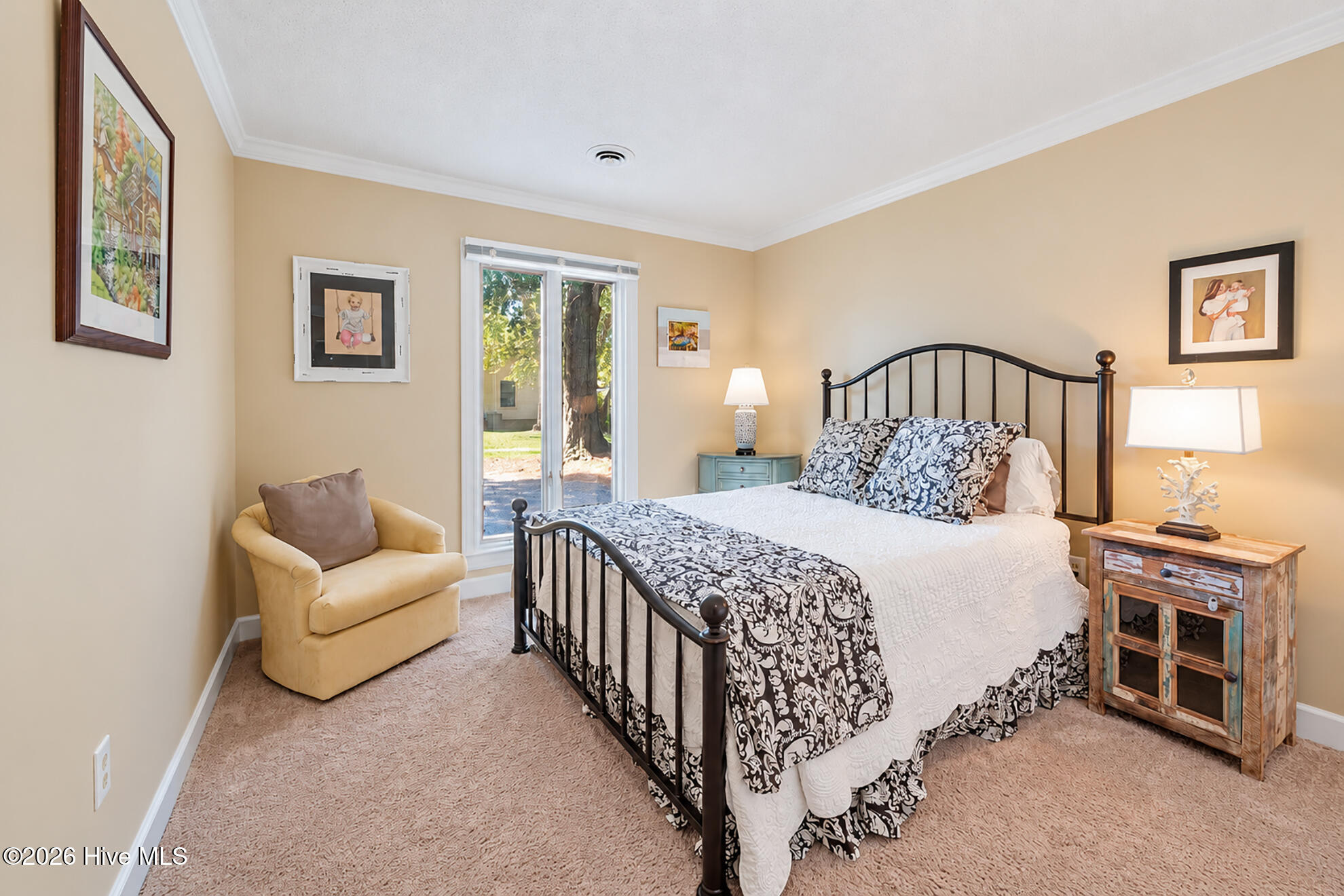 Bedroom with a black metal bed, patterned bedding, yellow armchair, and sliding glass door.