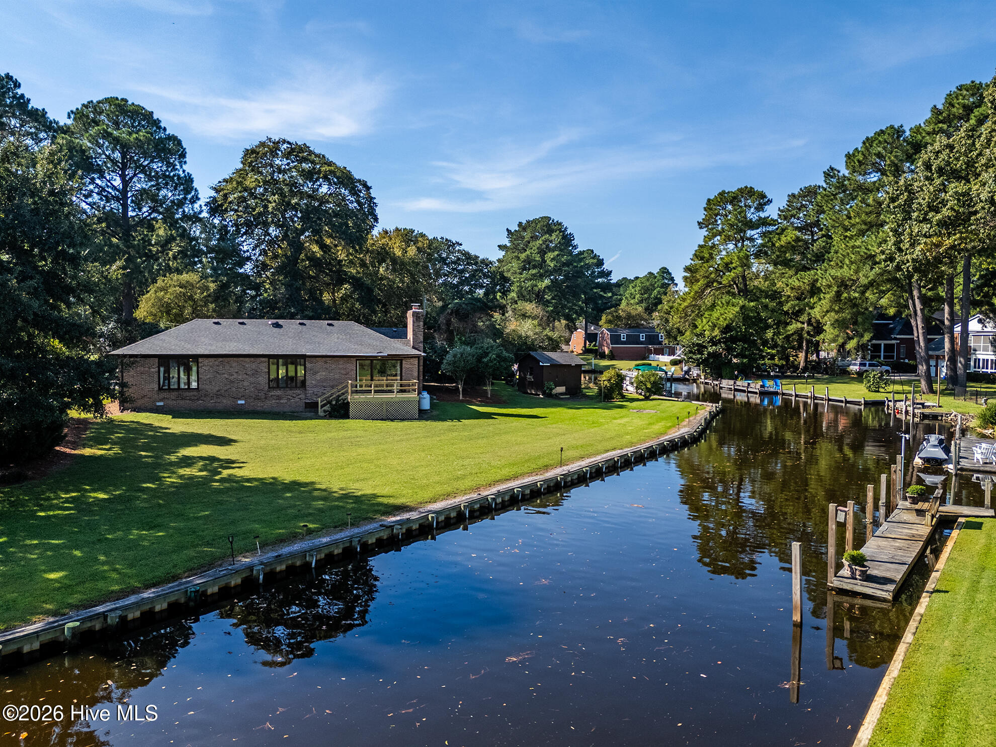 Brick ranch home beside a canal, with a broad lawn, curved bulkhead, and private dock.