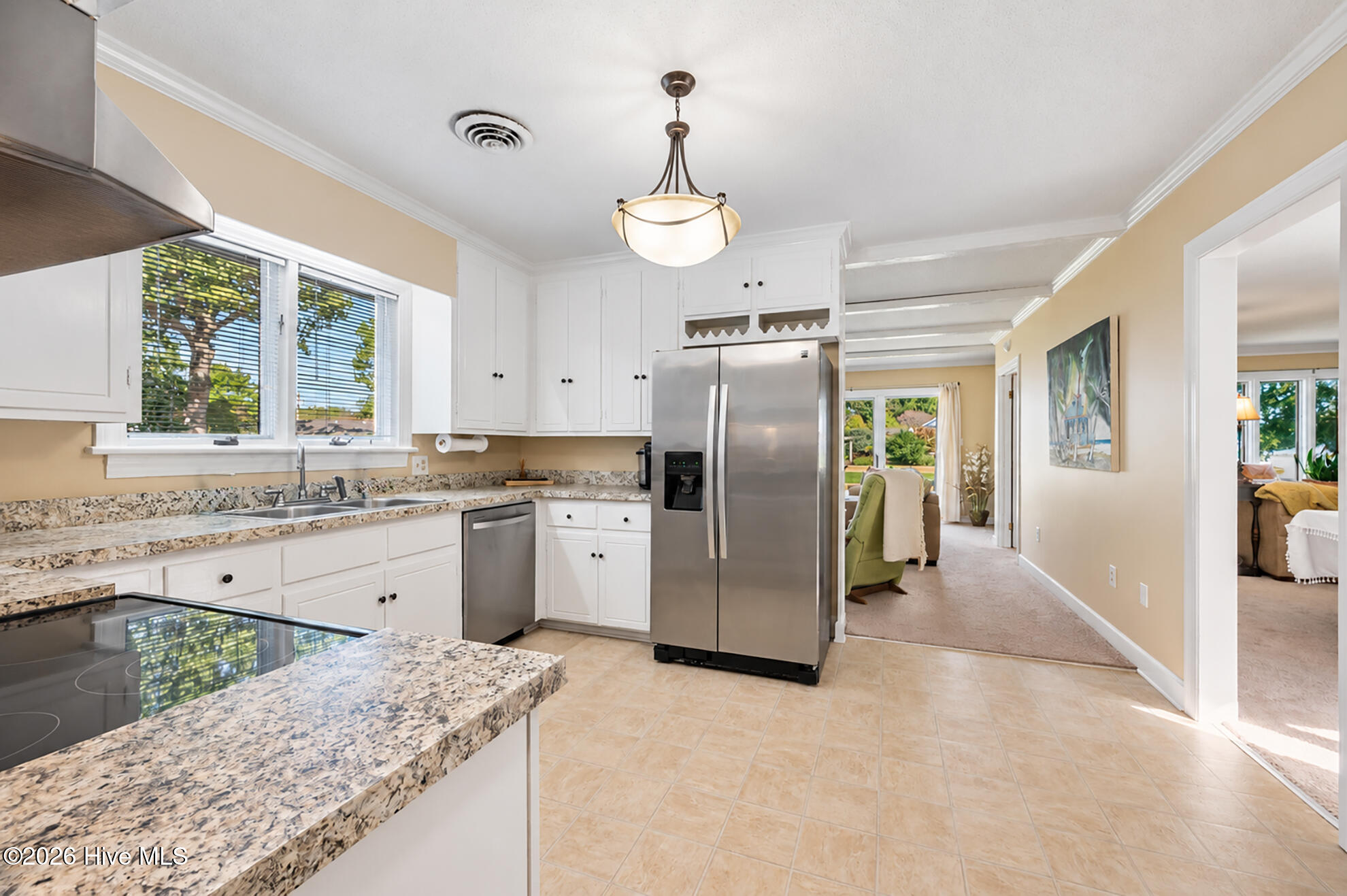 Bright kitchen with white cabinets, speckled stone counters, stainless appliances, and windows overlooking trees.