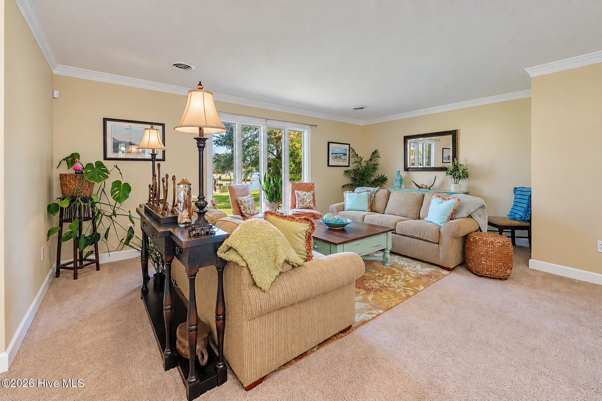 Living room with tan sofas, a mint-green coffee table, and tall windows overlooking trees.