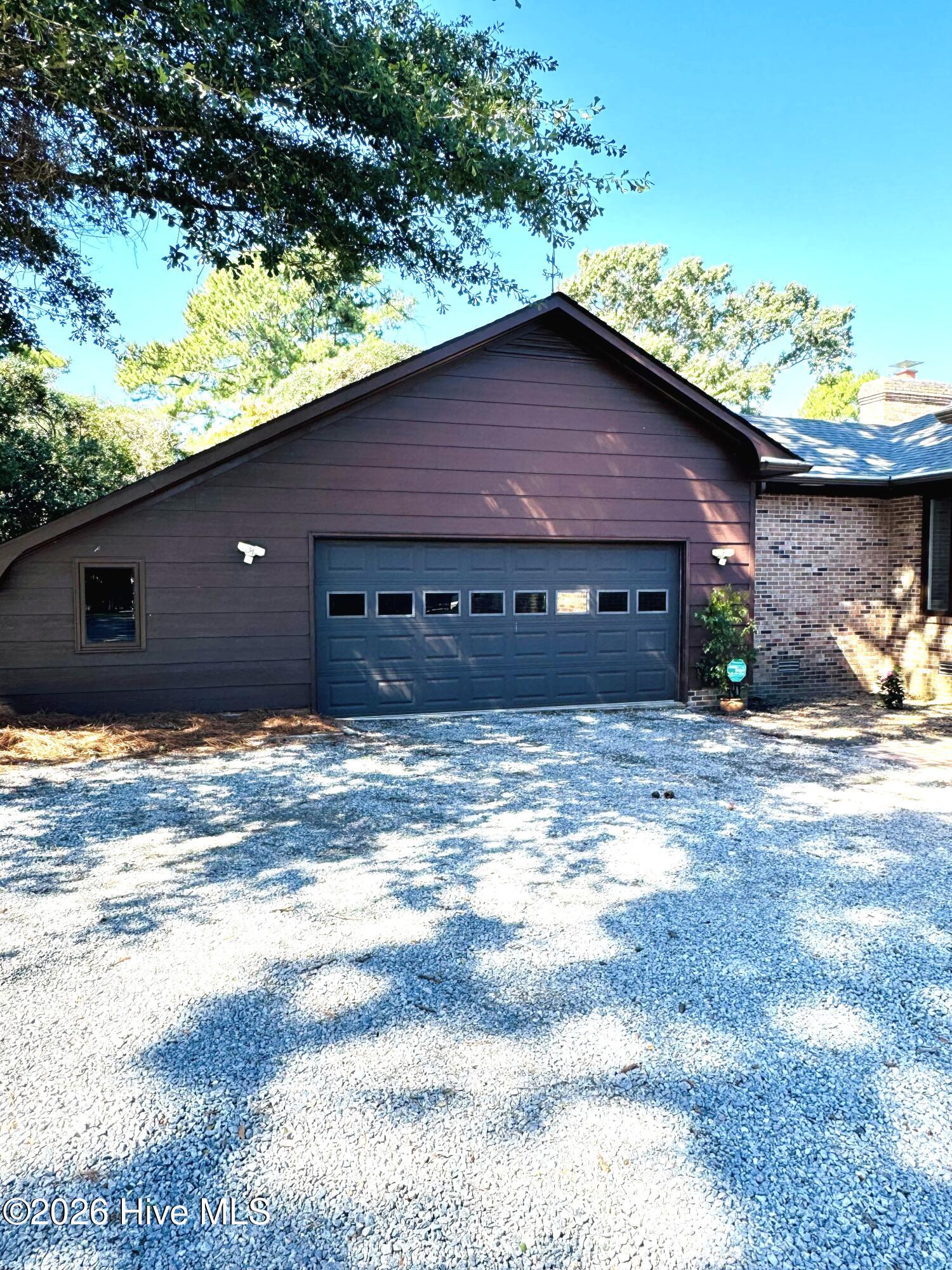 House exterior with a blue double garage door, brick wall, and wide gravel driveway.