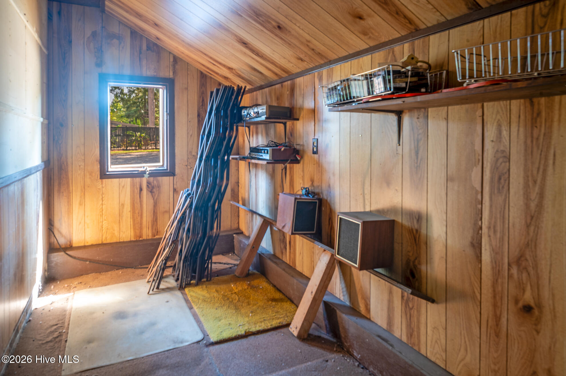 Wood-paneled storage room with a sloped ceiling, window, and shelves of equipment.