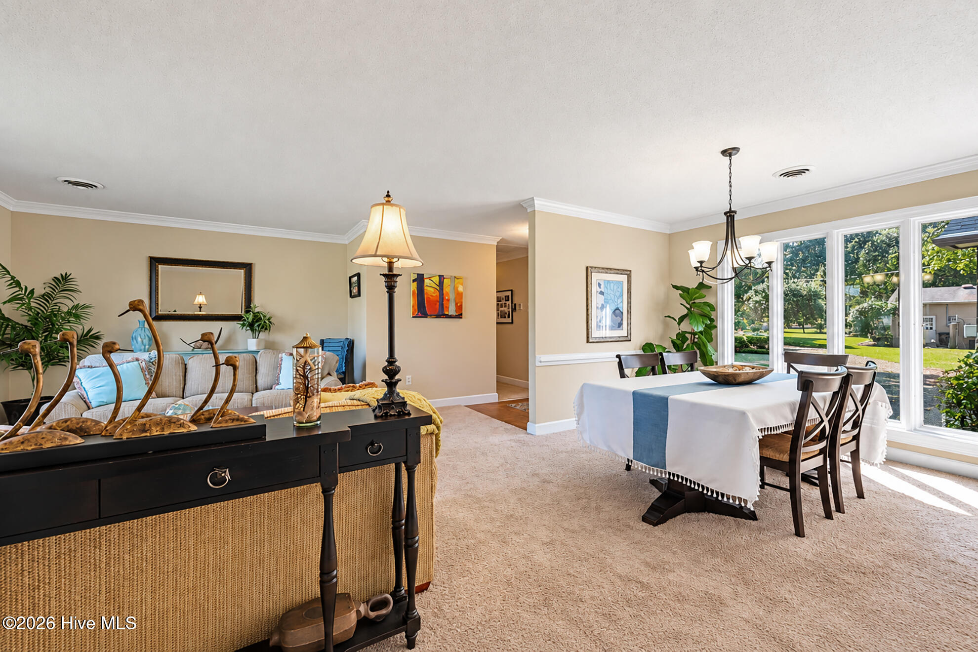 Furnished living and dining area with a set table beside large windows overlooking a green yard.