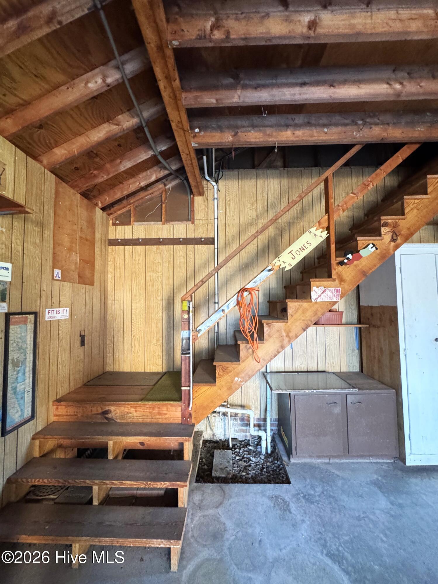Unfinished utility area with exposed rafters and a steep wooden staircase above open floor framing.