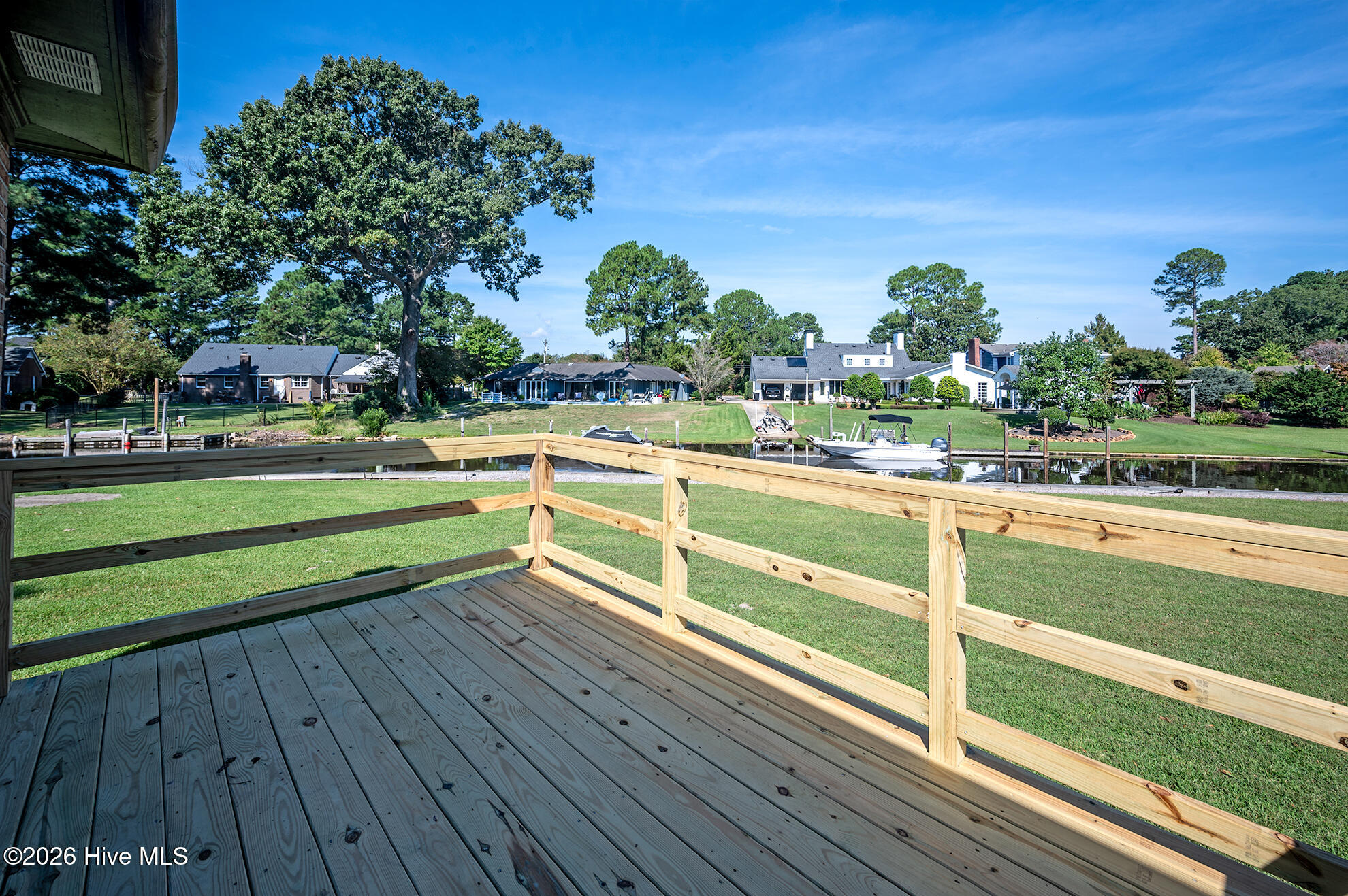 Wooden deck overlooking a canal, neighboring waterfront homes, docks, and a boat.