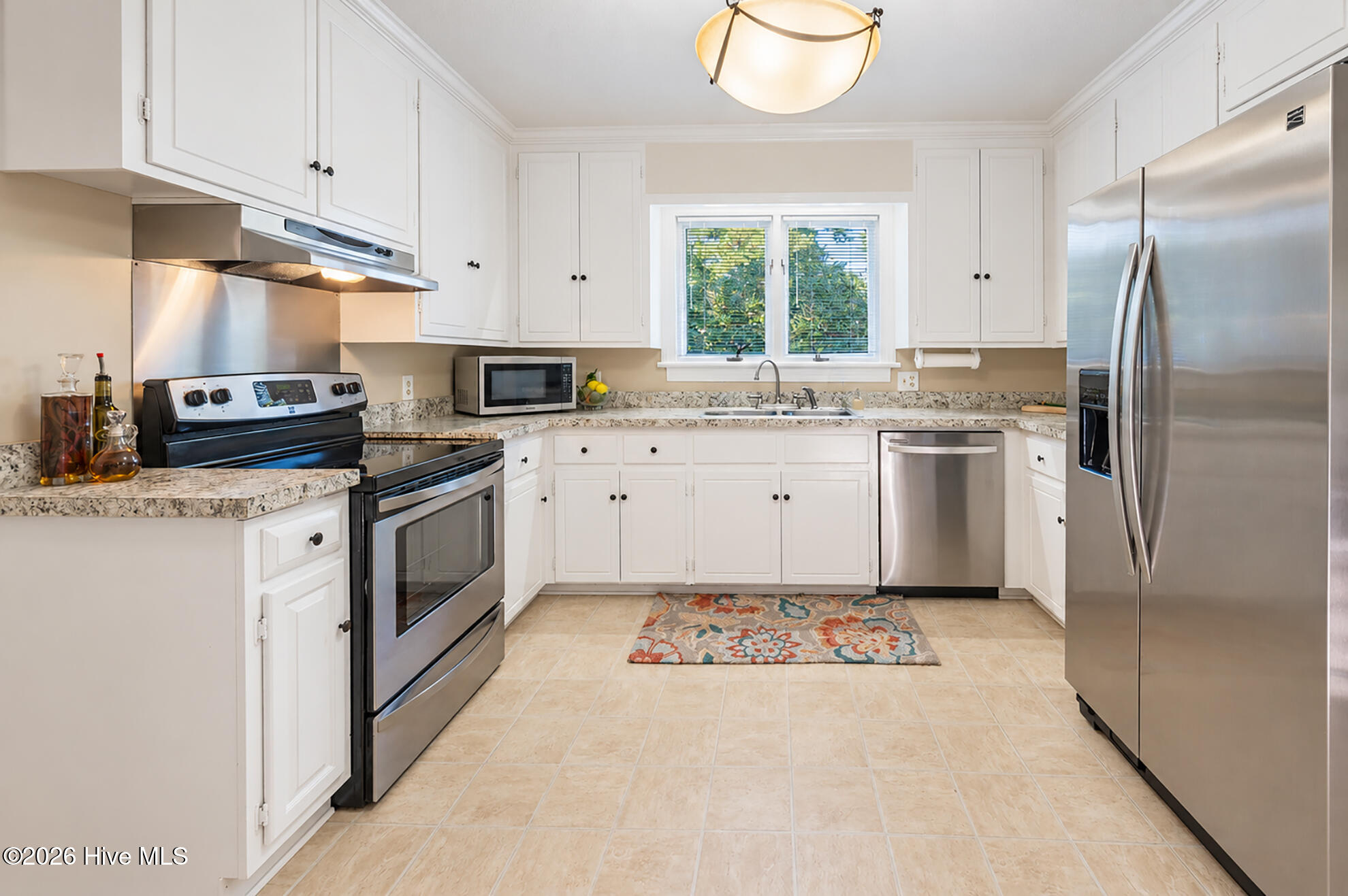 Bright kitchen with white cabinets, stainless steel appliances, and a colorful rug by the sink.
