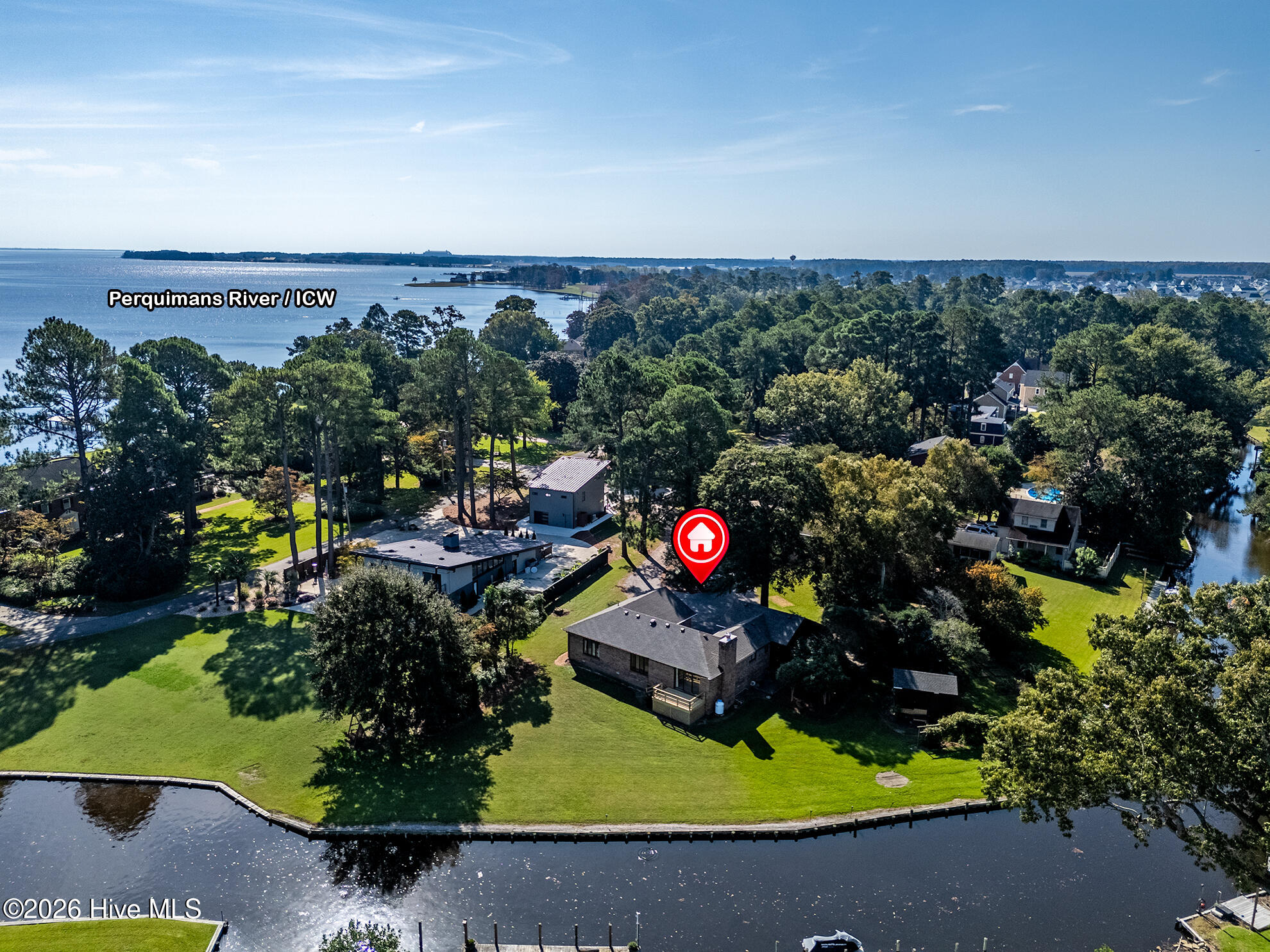 Aerial view of a waterfront home with a large lawn beside a canal and the Perquimans River beyond.