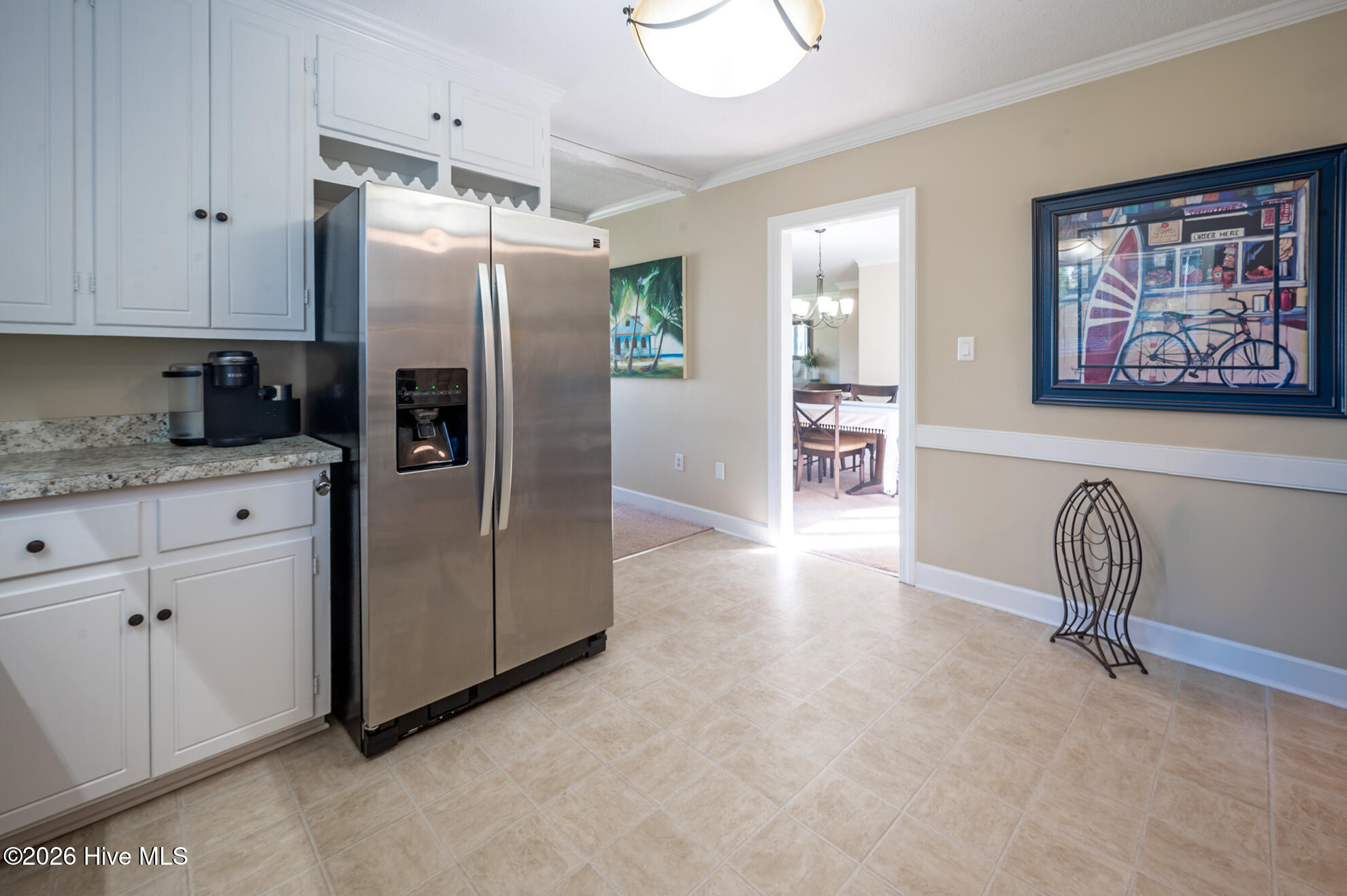 Kitchen with white cabinets, granite counters, stainless refrigerator, and a doorway to the dining room.
