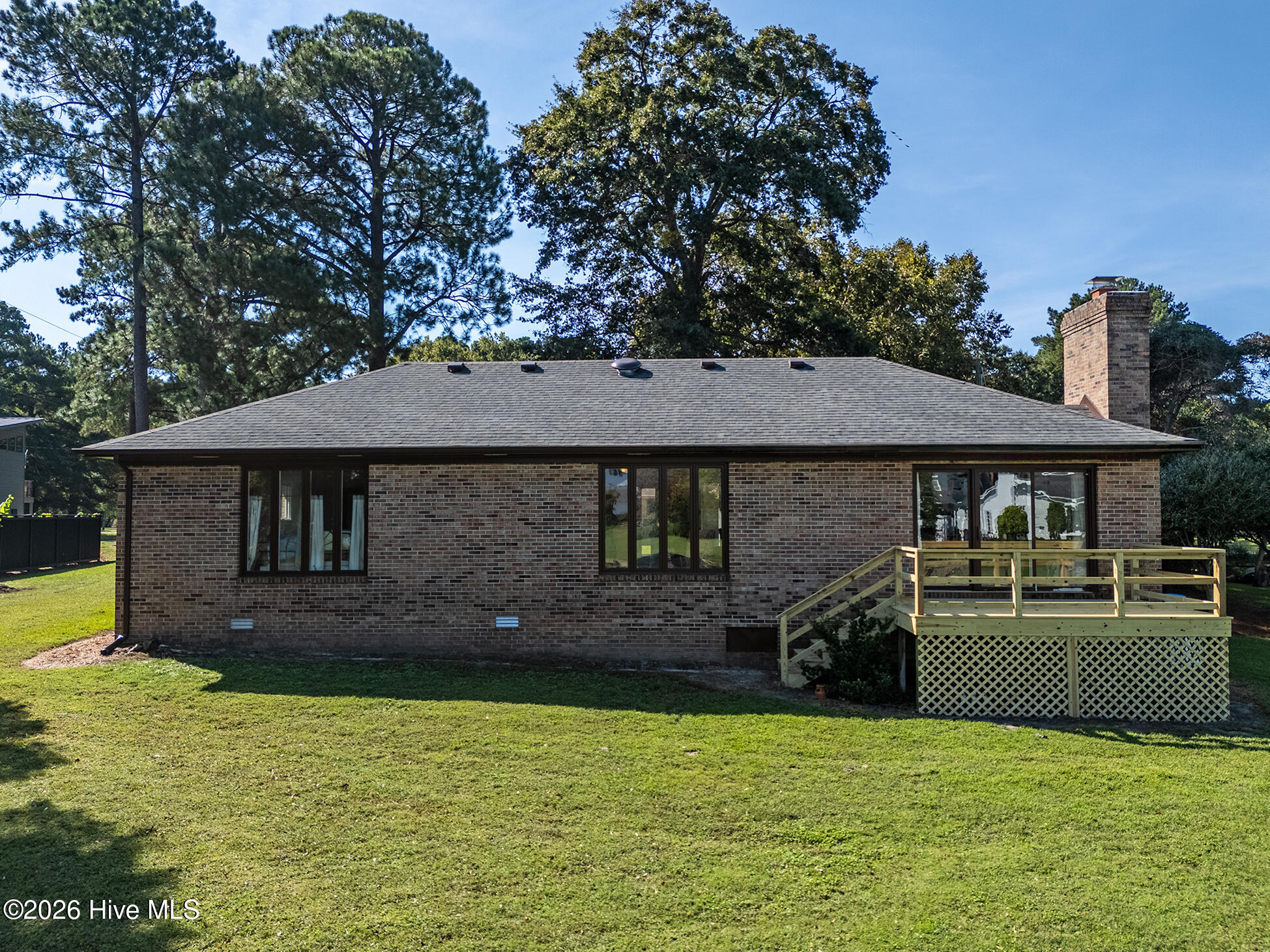 Brick ranch house with a raised wooden deck, lattice skirting, and a broad green lawn.