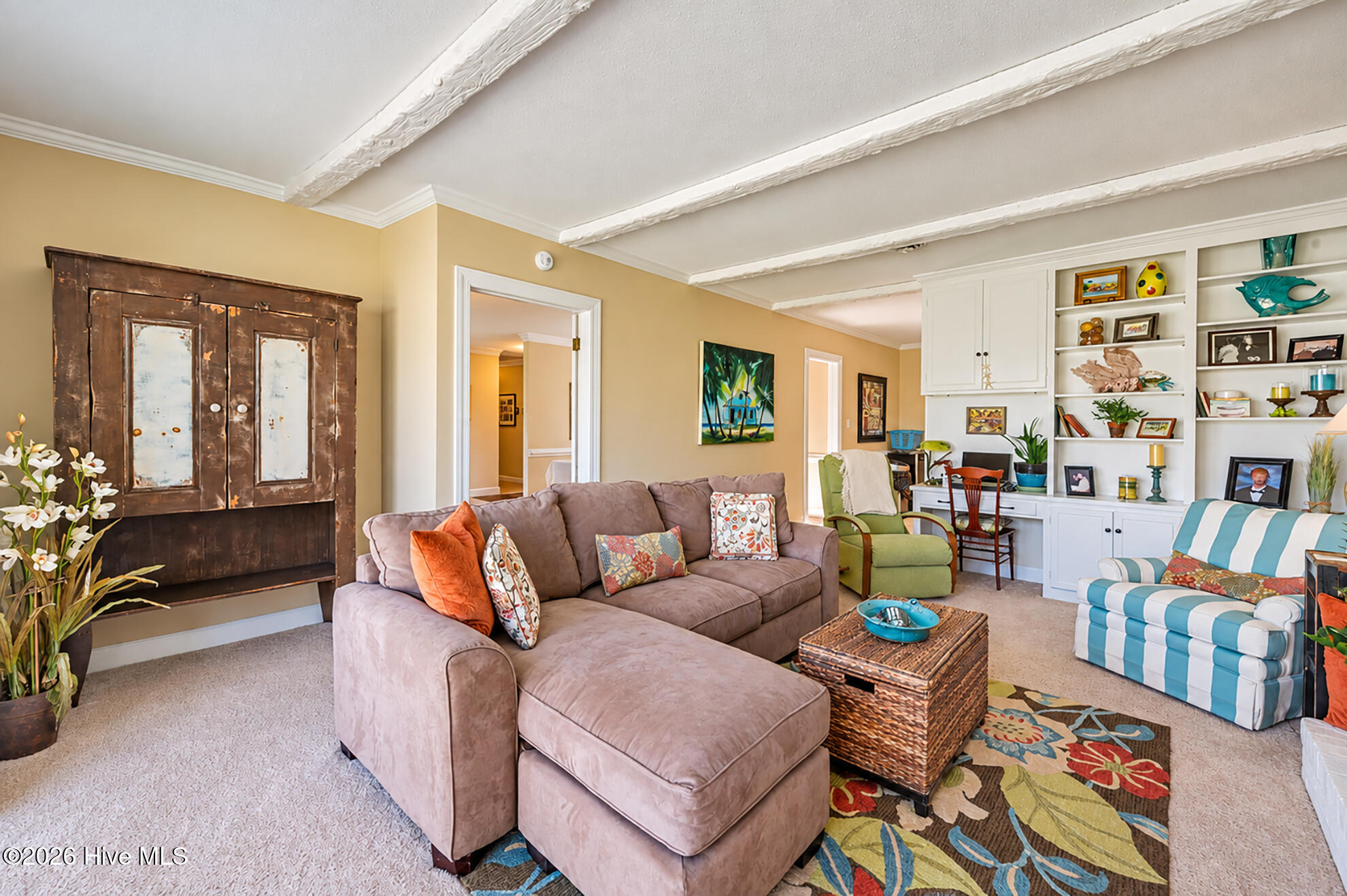 Living room with a taupe sectional, striped armchair, distressed cabinet, and white built-in shelving.