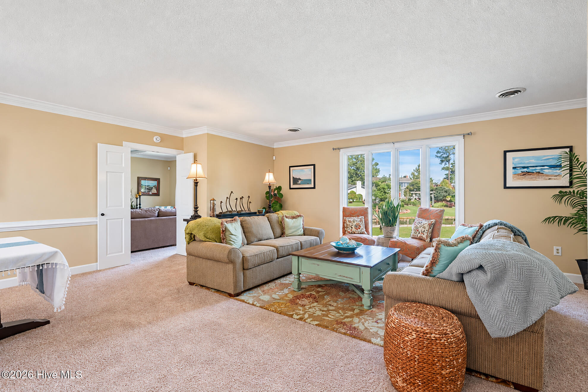 Living room with sofas, coastal artwork, and large windows overlooking a landscaped yard.