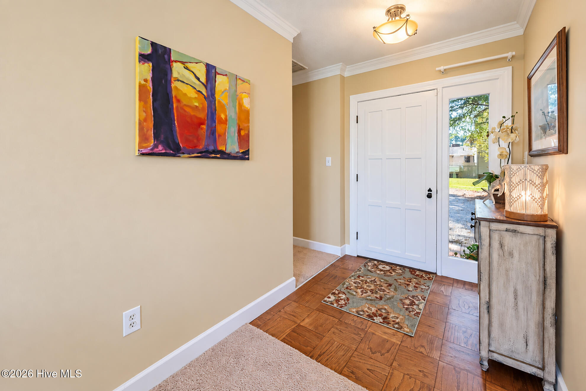 Entry foyer with a white paneled door, wood-pattern flooring, colorful abstract art, and a console table.
