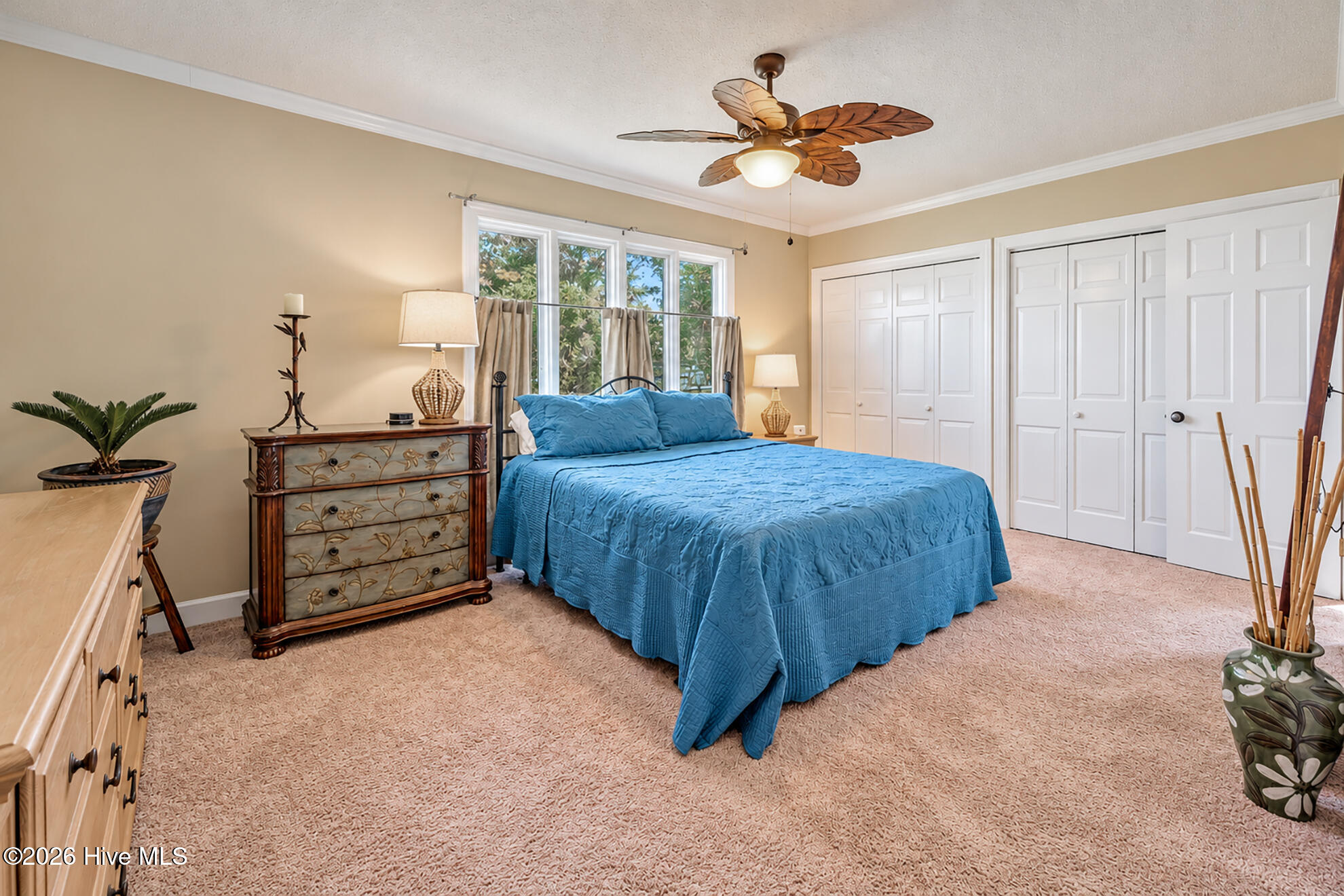 Bedroom with a blue quilted bed, decorative wooden dresser, and white closet doors.