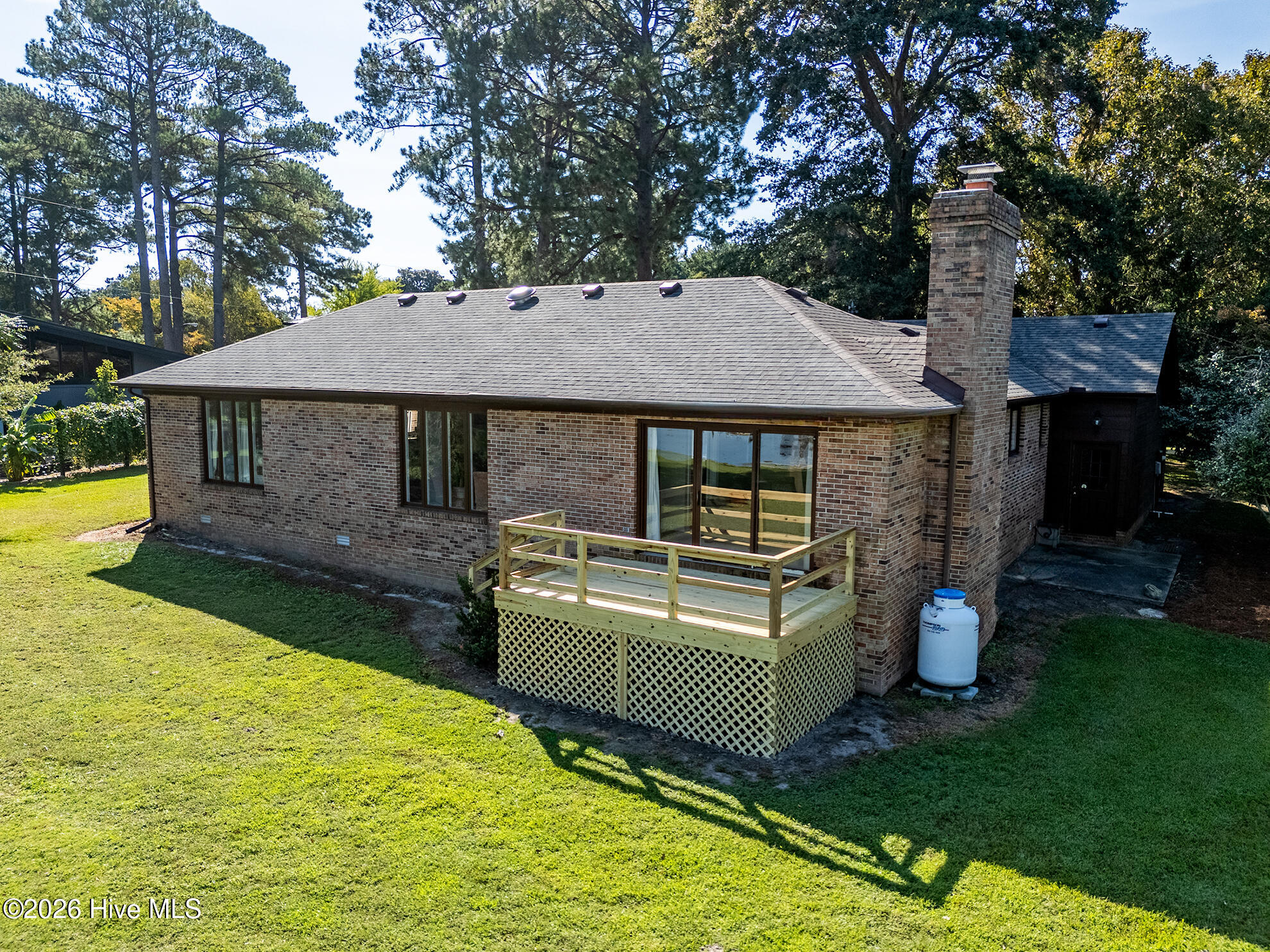 Brick house with a raised wooden deck, tall chimney, and mature trees behind it.