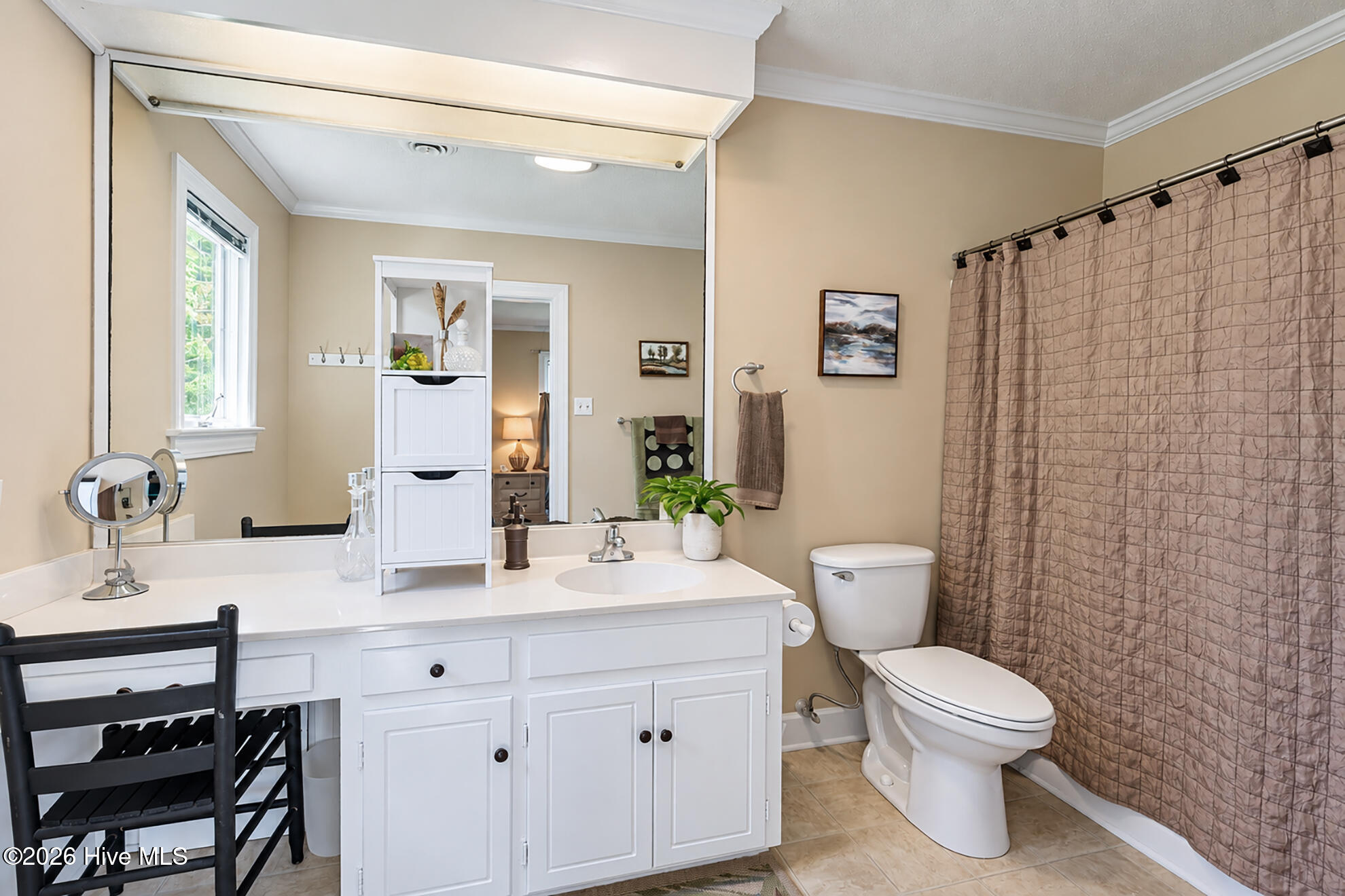 Bathroom with a white vanity and large mirror, toilet, and tub behind a brown patterned shower curtain.