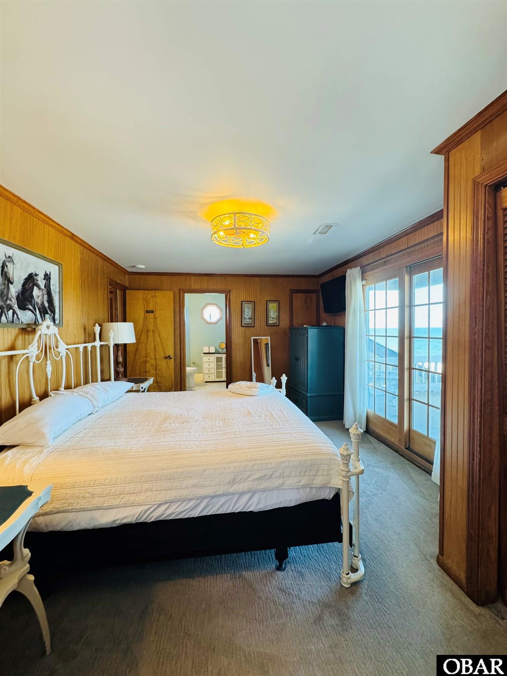 Bedroom with a white bed, wood-paneled walls, and glass doors overlooking the ocean.
