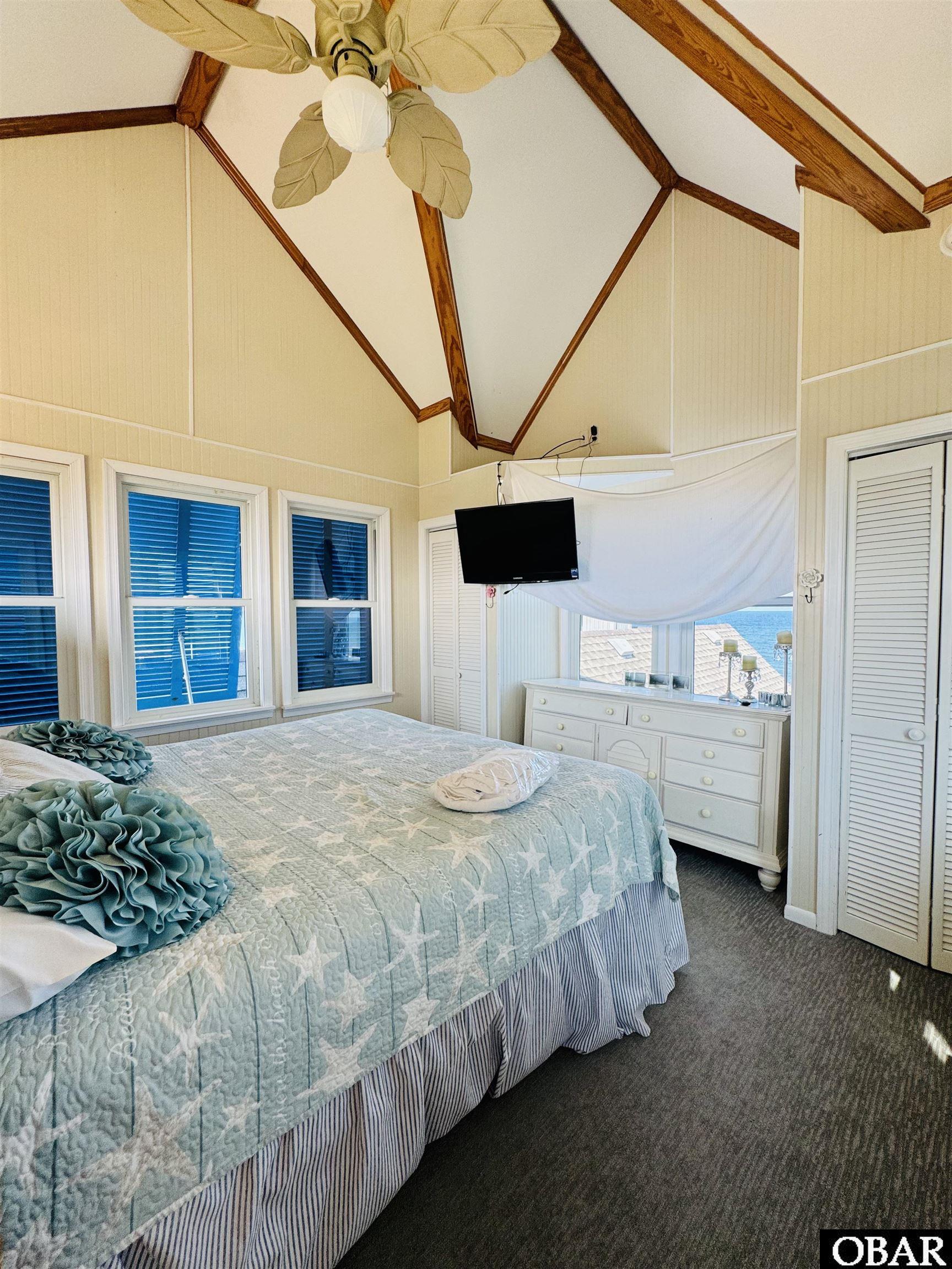 Coastal bedroom with an aqua starfish quilt, vaulted wood-beam ceiling, and ocean views through the windows.