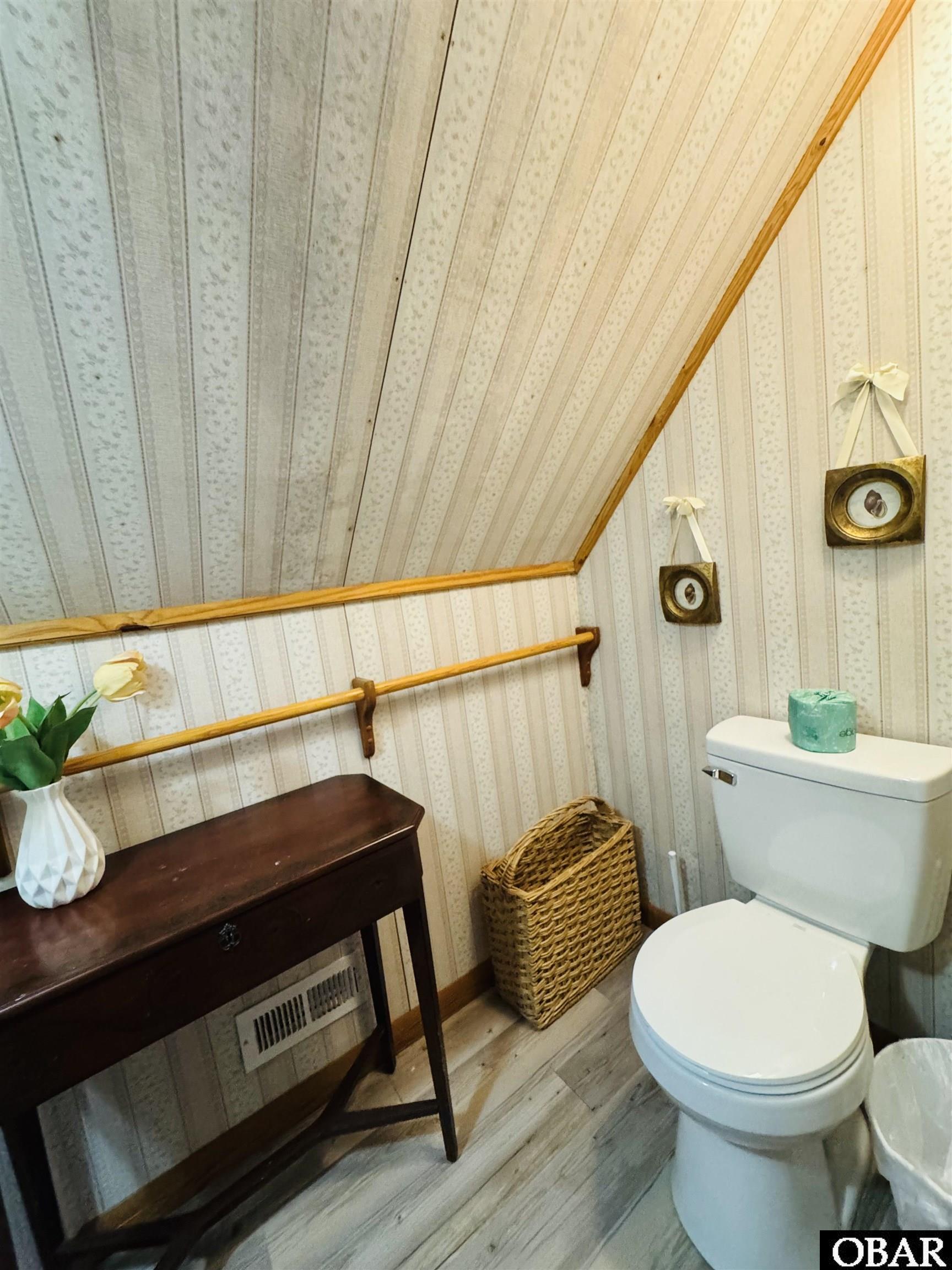 Bathroom with a white toilet beneath a sloped ceiling and a dark wooden console table.
