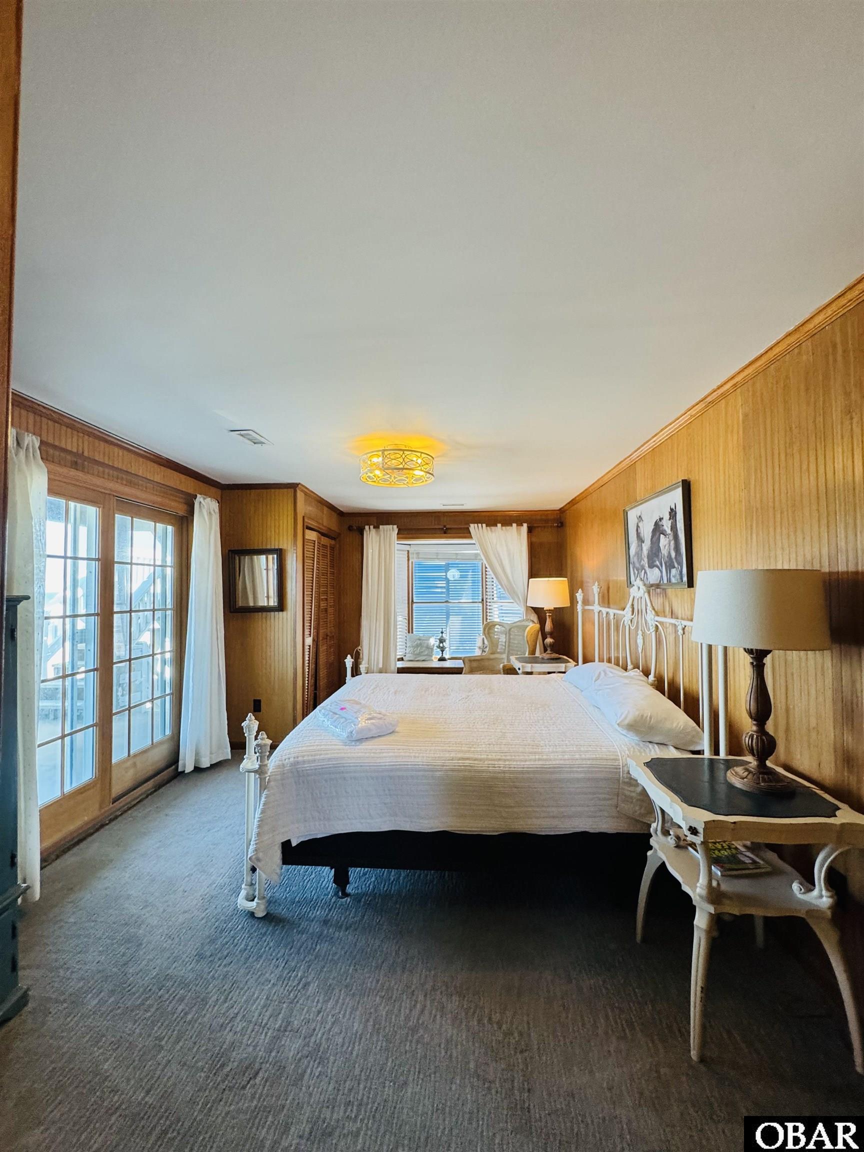 Bedroom with a white iron bed, wood-paneled walls, and French doors.