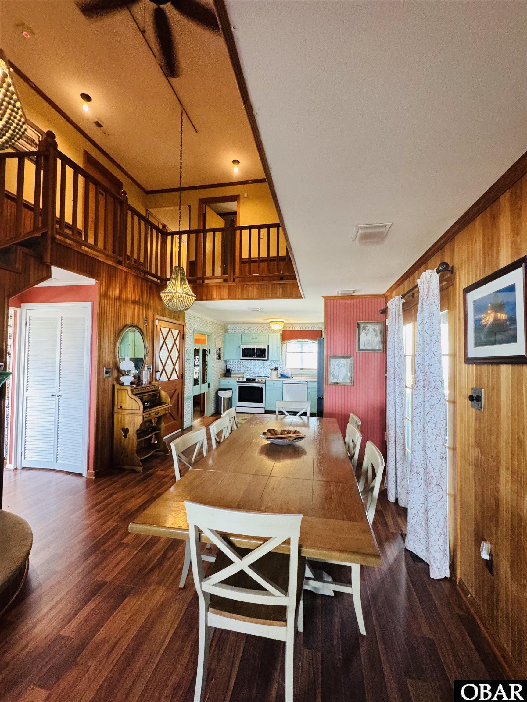 Dining room with a long wooden table, loft railing, and turquoise kitchen.