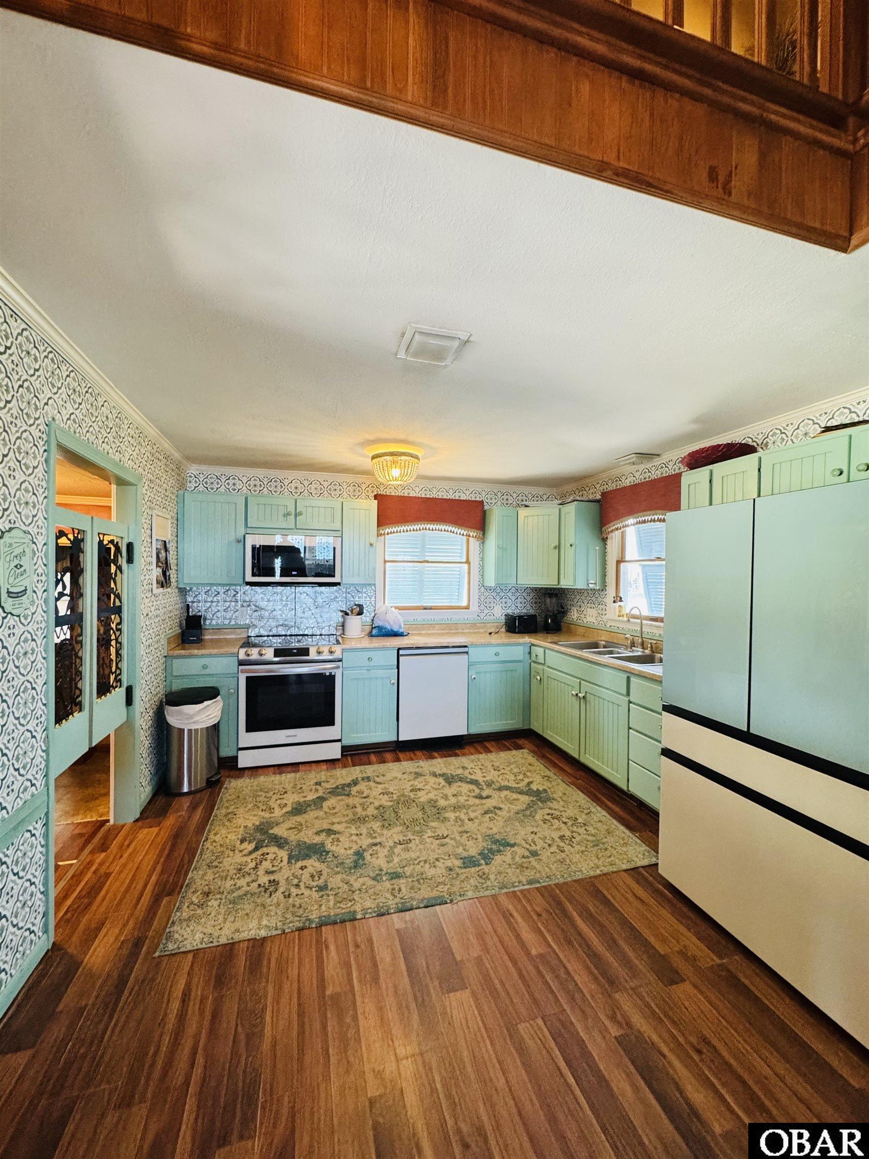 Kitchen with mint-green cabinets, patterned wallpaper, and a large refrigerator.