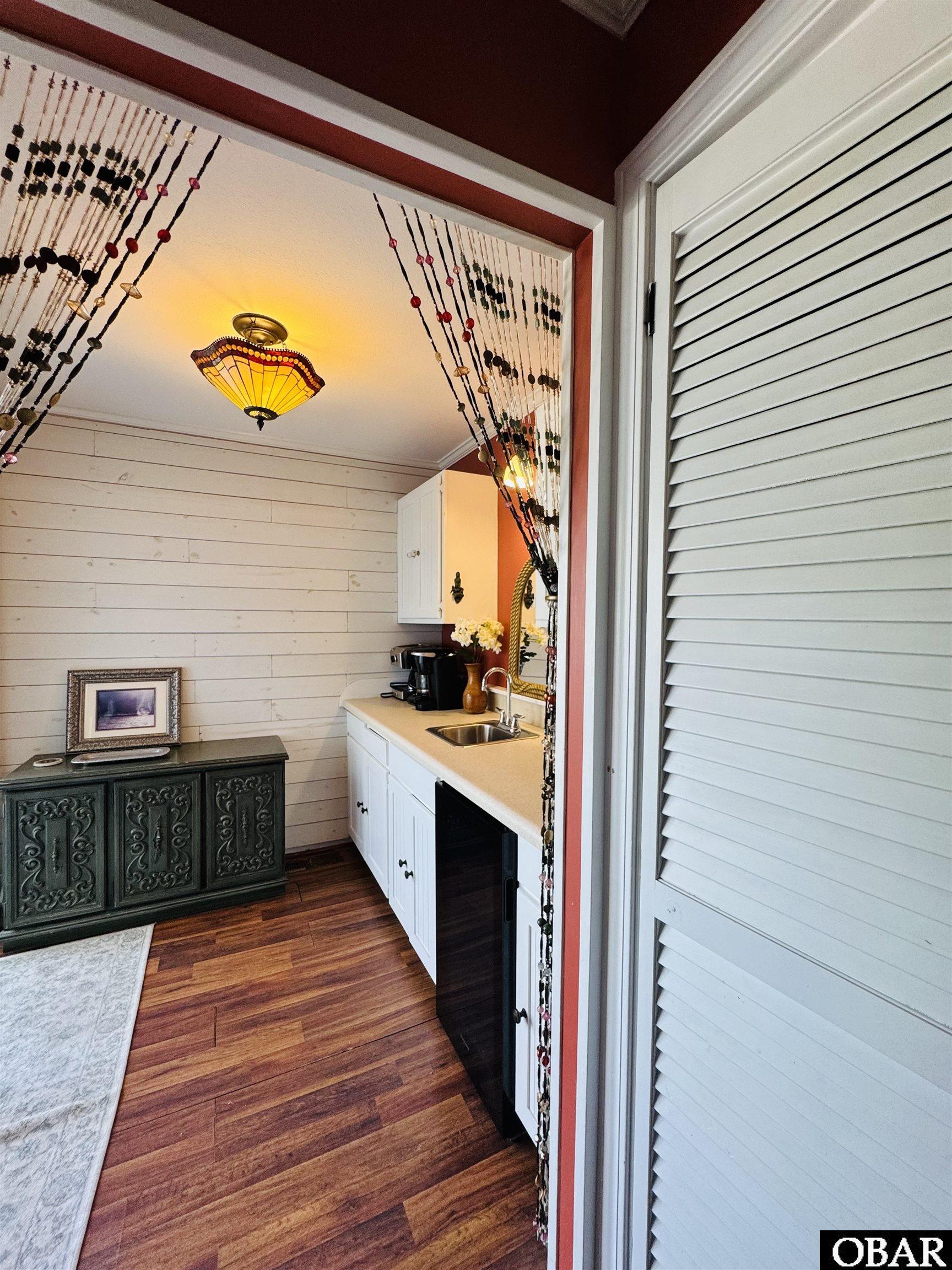 Compact kitchen with white cabinets, a sink, wood flooring, and a colorful pendant light.