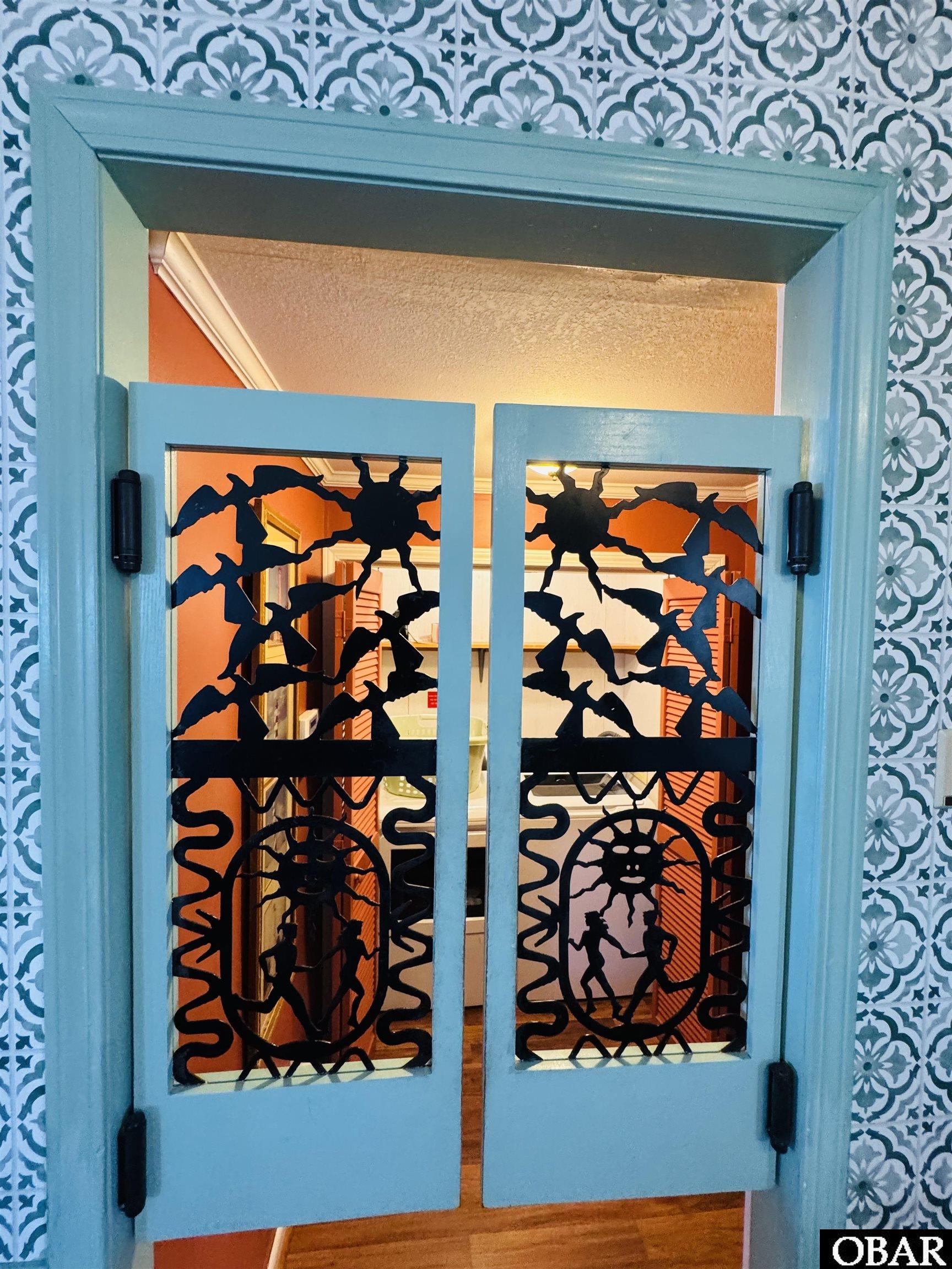 Turquoise saloon doors with black spiderweb cutouts set in patterned wallpaper.
