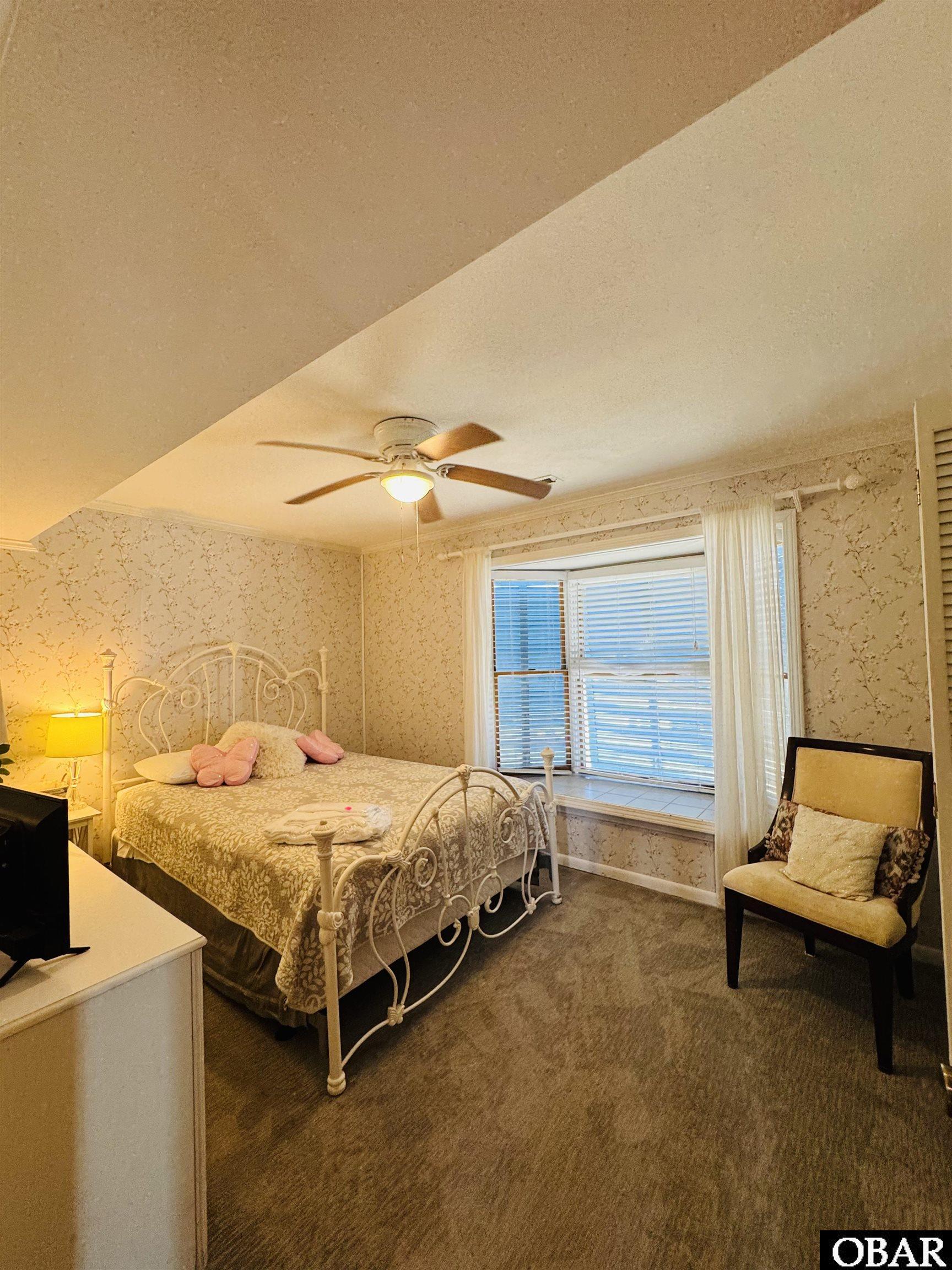Bedroom with an ornate white metal bed, floral wallpaper, and a large window with blinds.