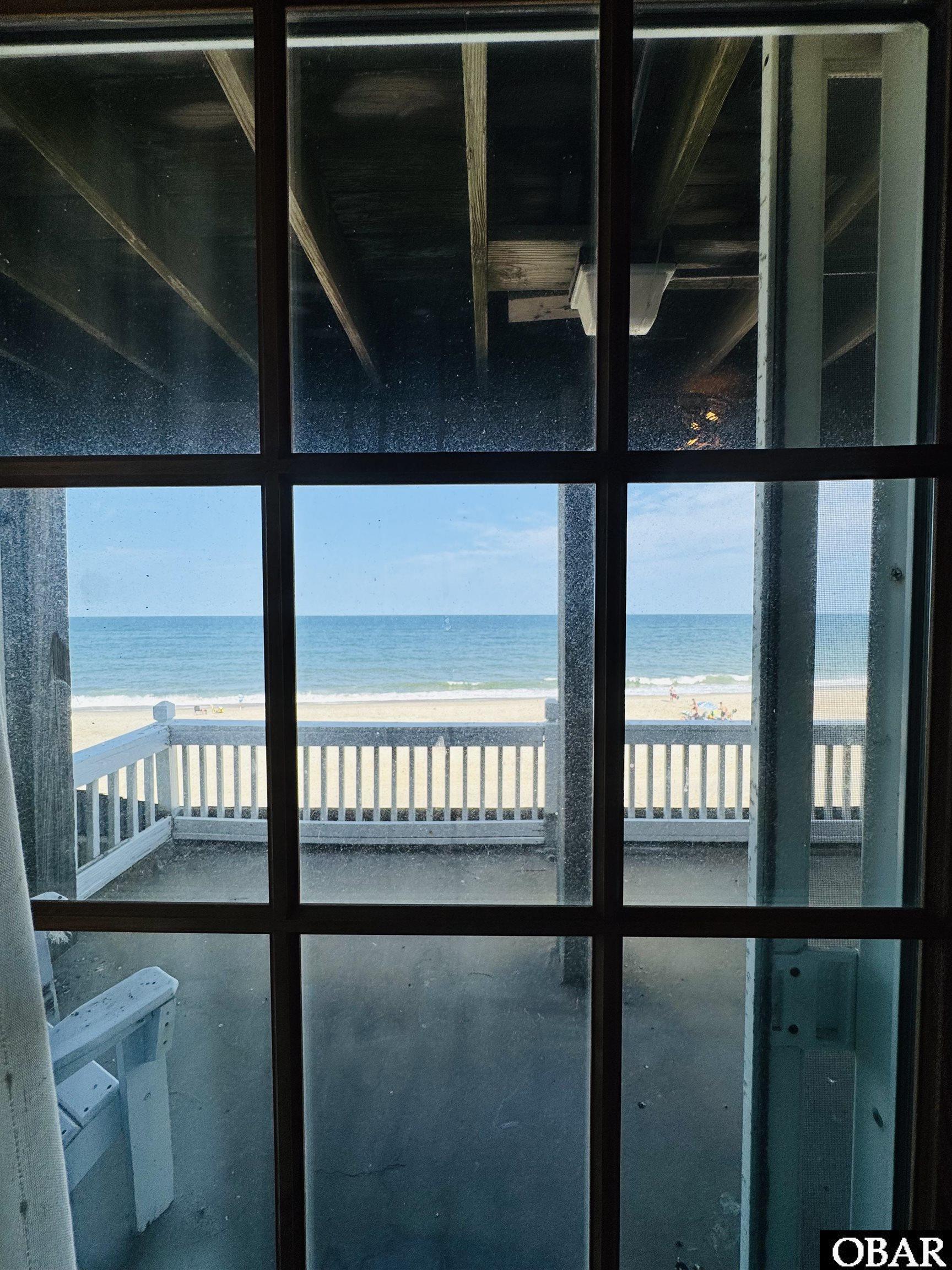 Ocean and sandy beach viewed through a glass door from a deck-facing room.