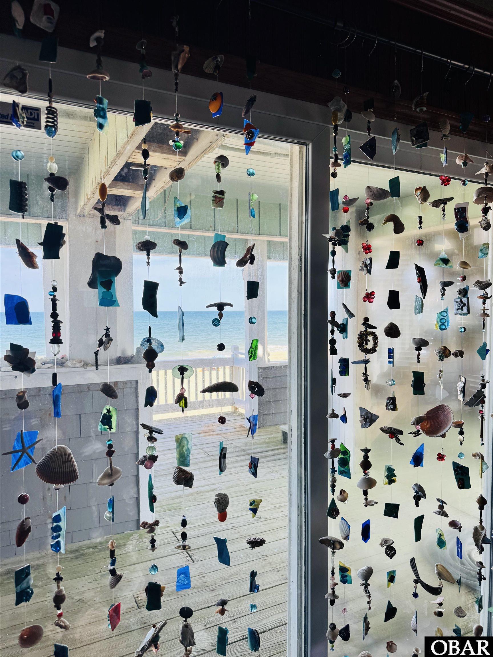 Hanging glass and shell decorations frame an ocean view from a home’s deck doors.