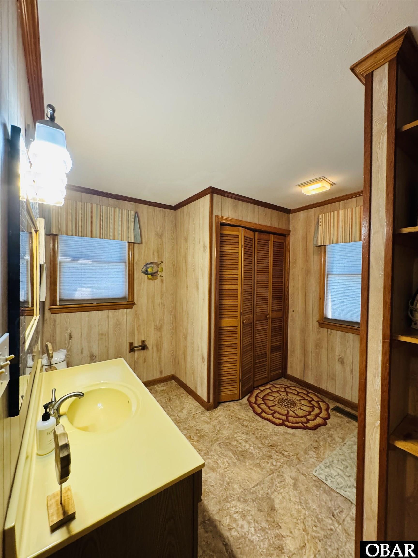 Bathroom with a yellow vanity, wood-paneled walls, louvered closet doors, and a patterned rug.