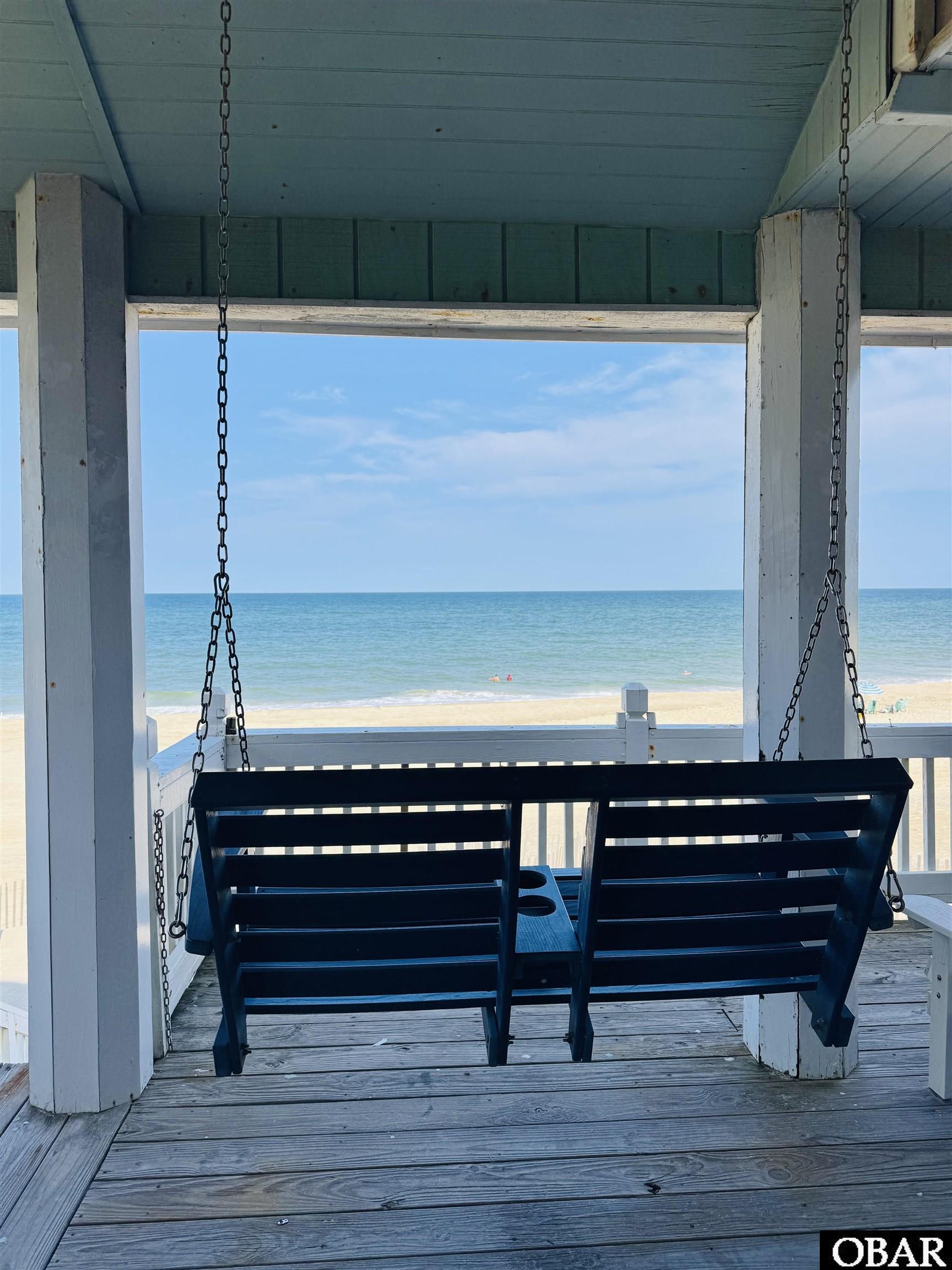Covered porch with a hanging bench swing overlooking the beach and ocean.