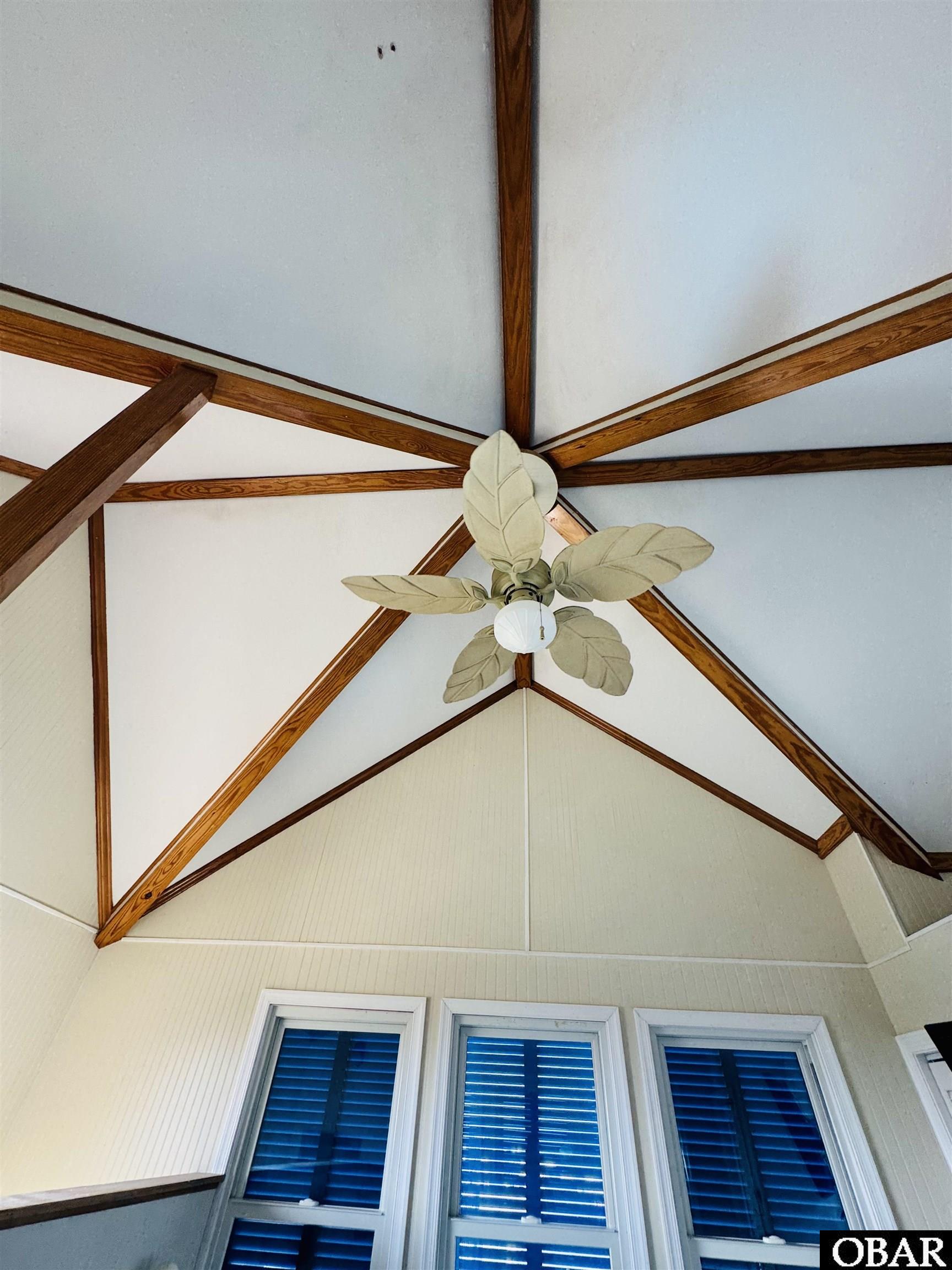 Vaulted interior ceiling with exposed wooden trusses, a leaf-shaped fan, and tall shuttered windows.