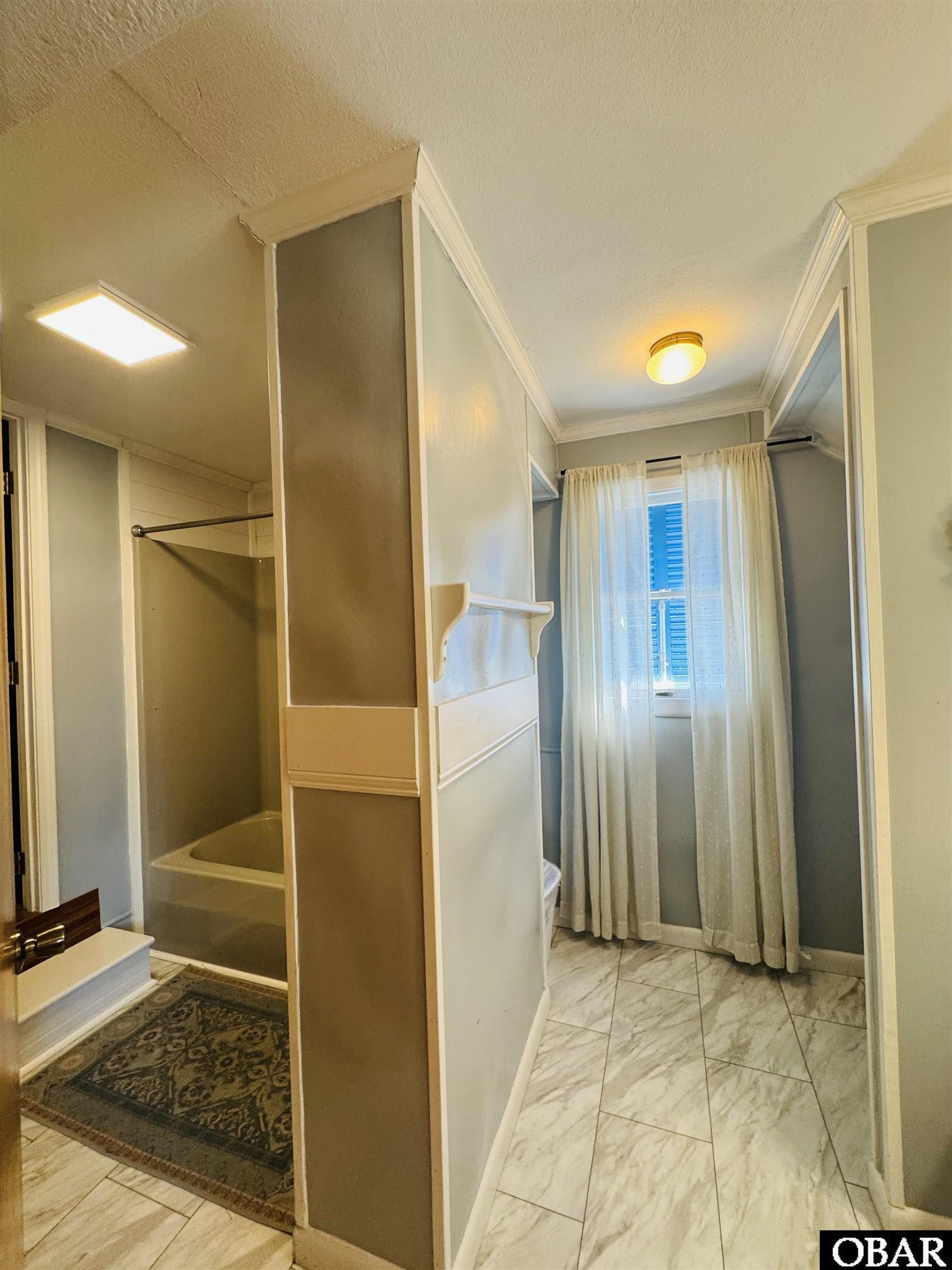 Bathroom with a partitioned tub and shower, marble-look tile floor, and curtained window.
