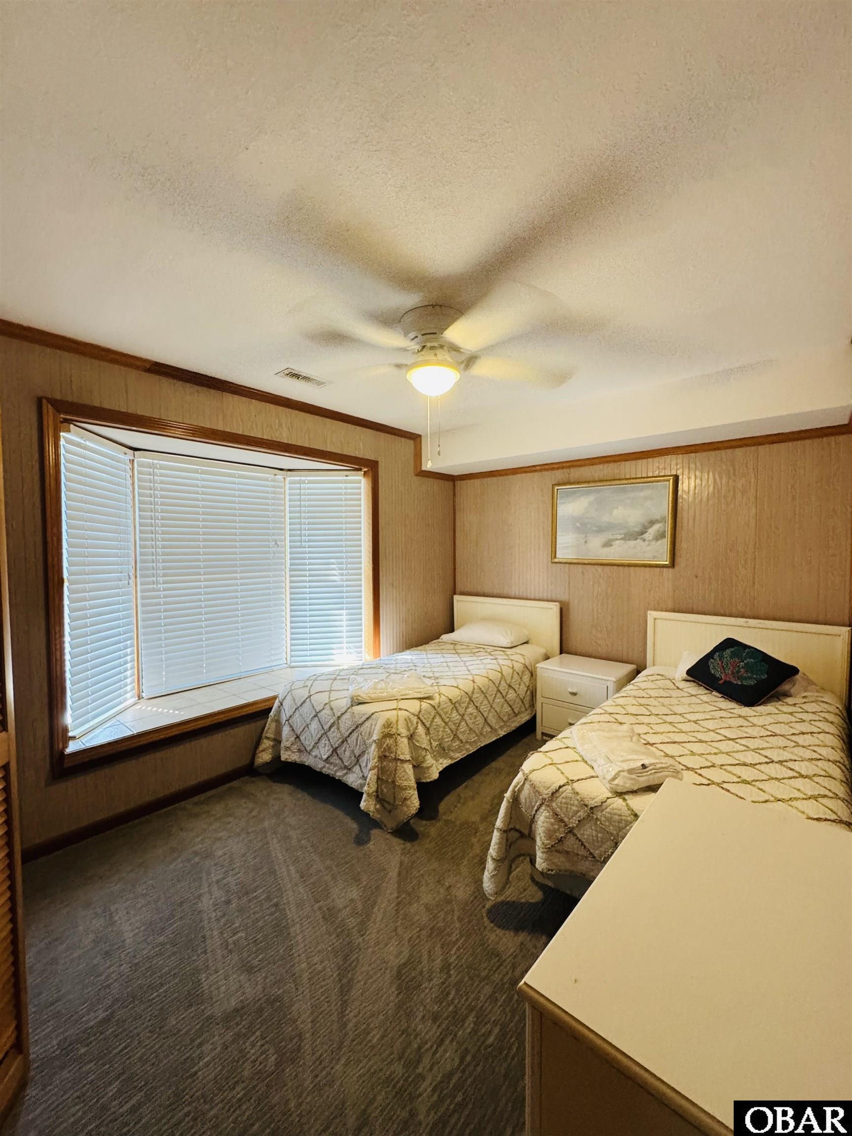 Bedroom with two single beds beside a large bay window with closed blinds.