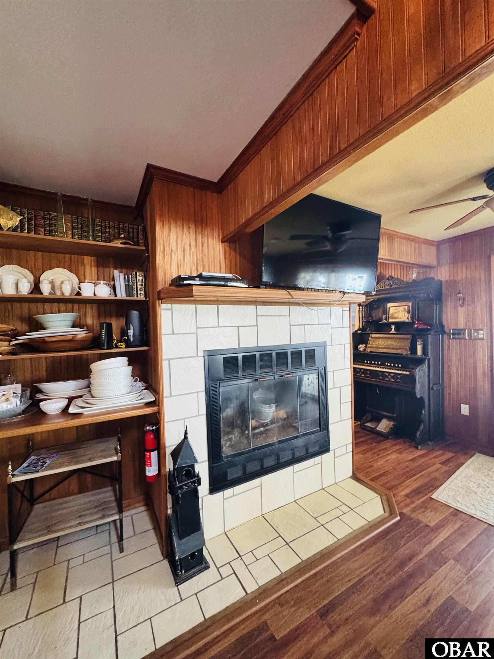 Living room with a white tiled fireplace, built-in shelves, wood paneling, and a television above the mantel.