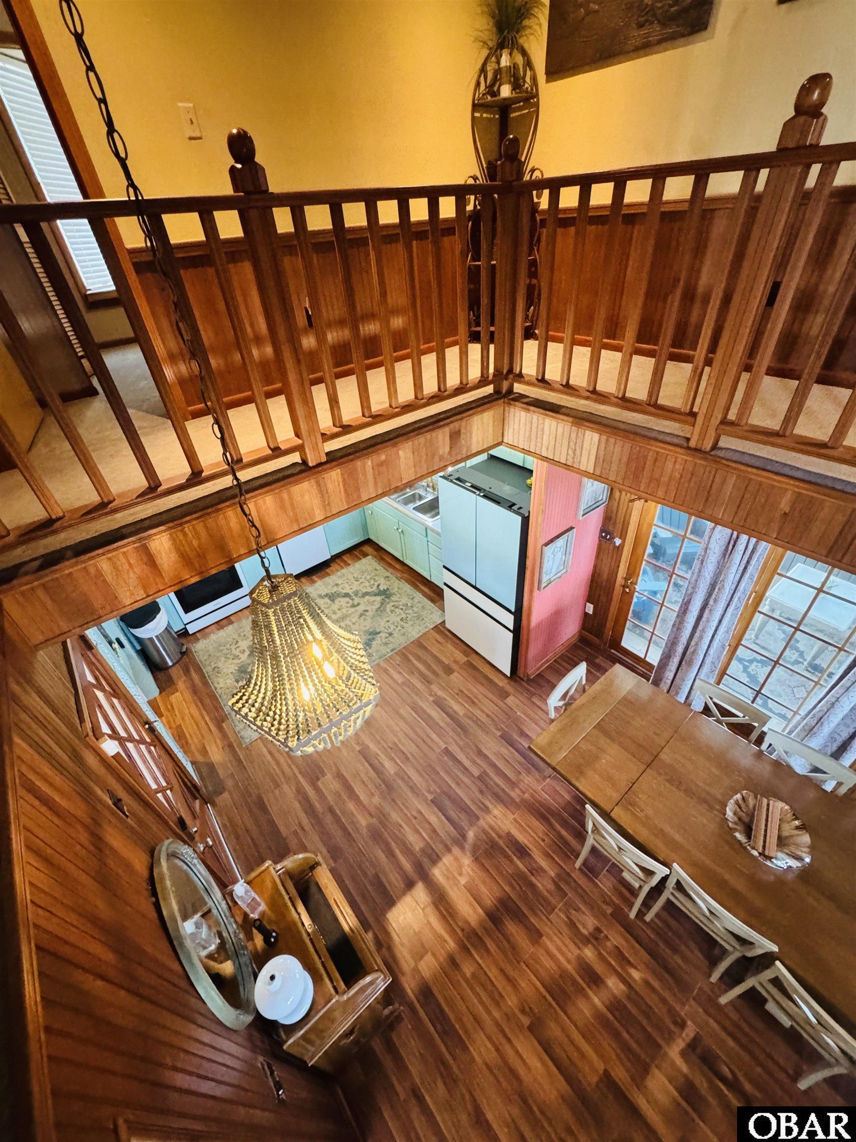 Loft view over a wood-paneled kitchen and dining area with a chandelier and hardwood floors.