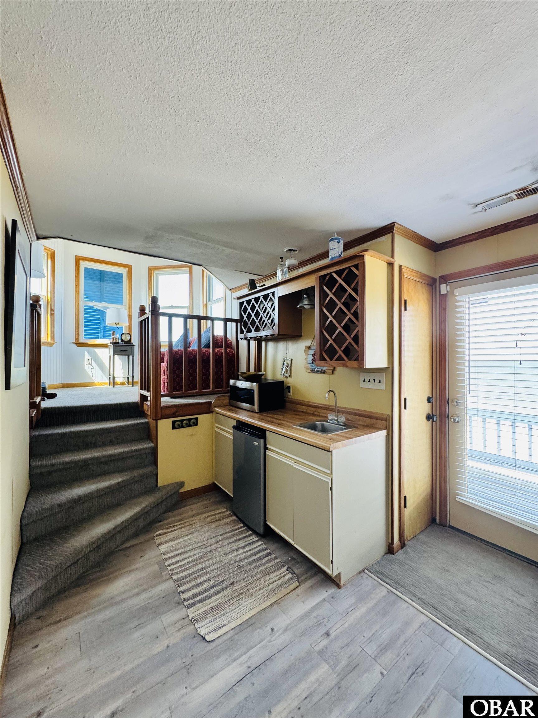 Compact kitchenette with wood counter and wine racks beside carpeted steps to a raised sleeping area.