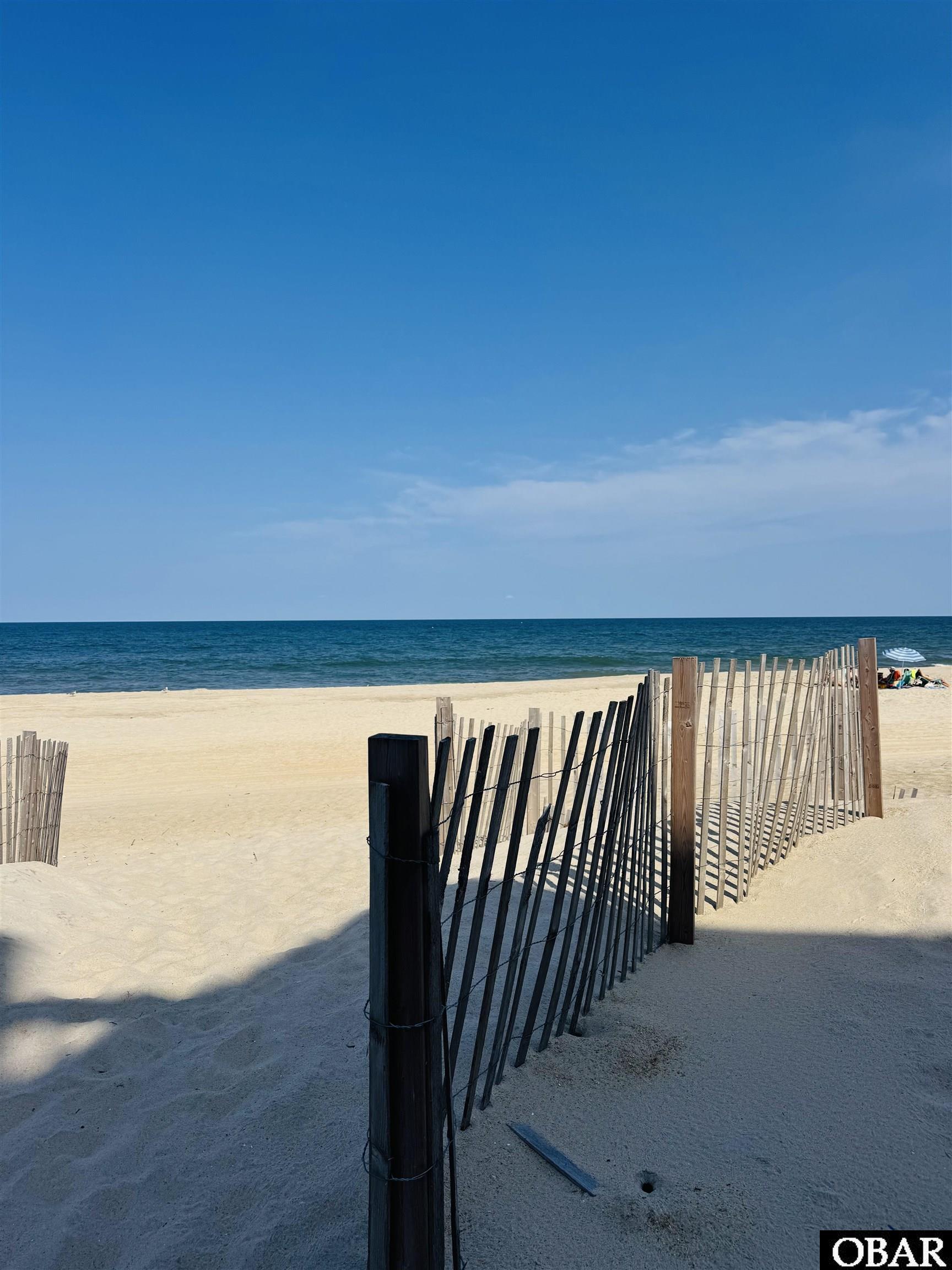 Sandy beach and blue ocean beyond a slatted wooden sand fence.
