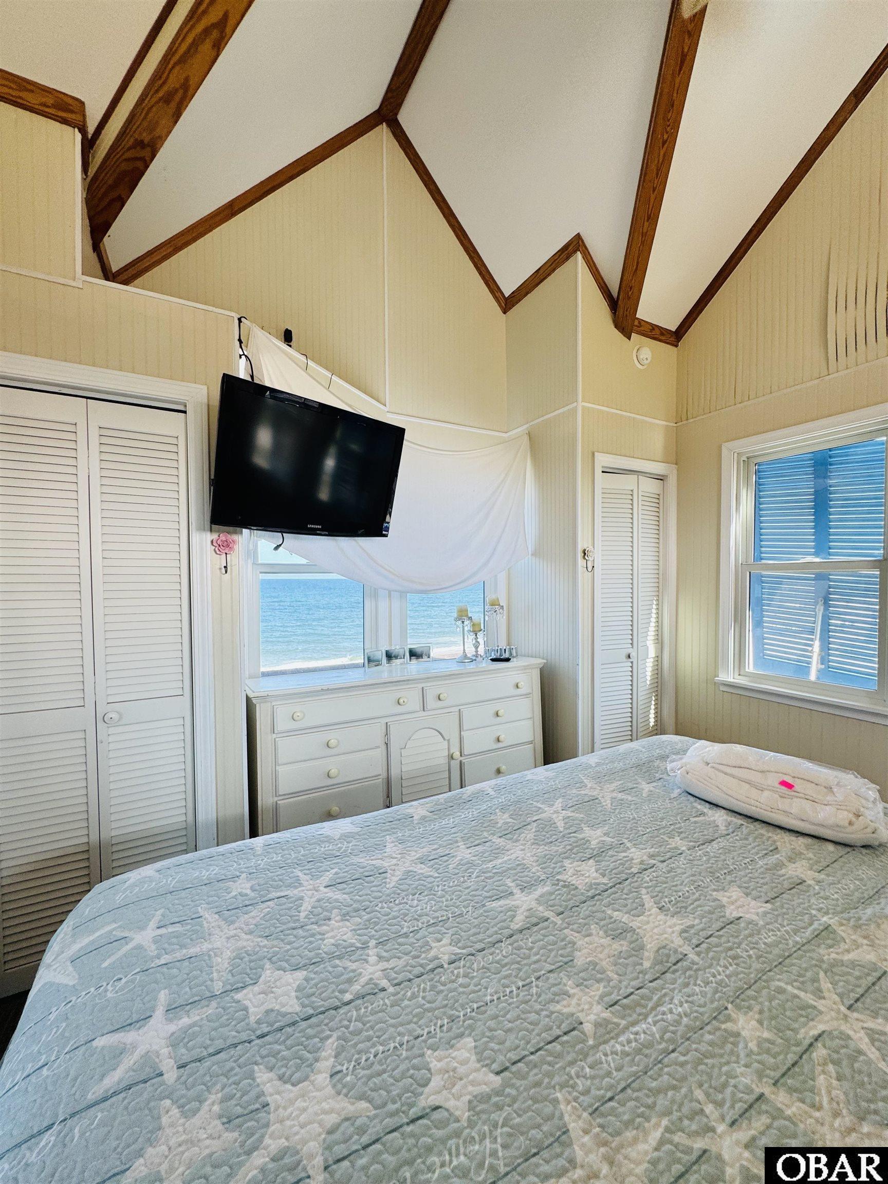 Bedroom with vaulted wood-beamed ceiling, starfish bedspread, and ocean visible through the window.