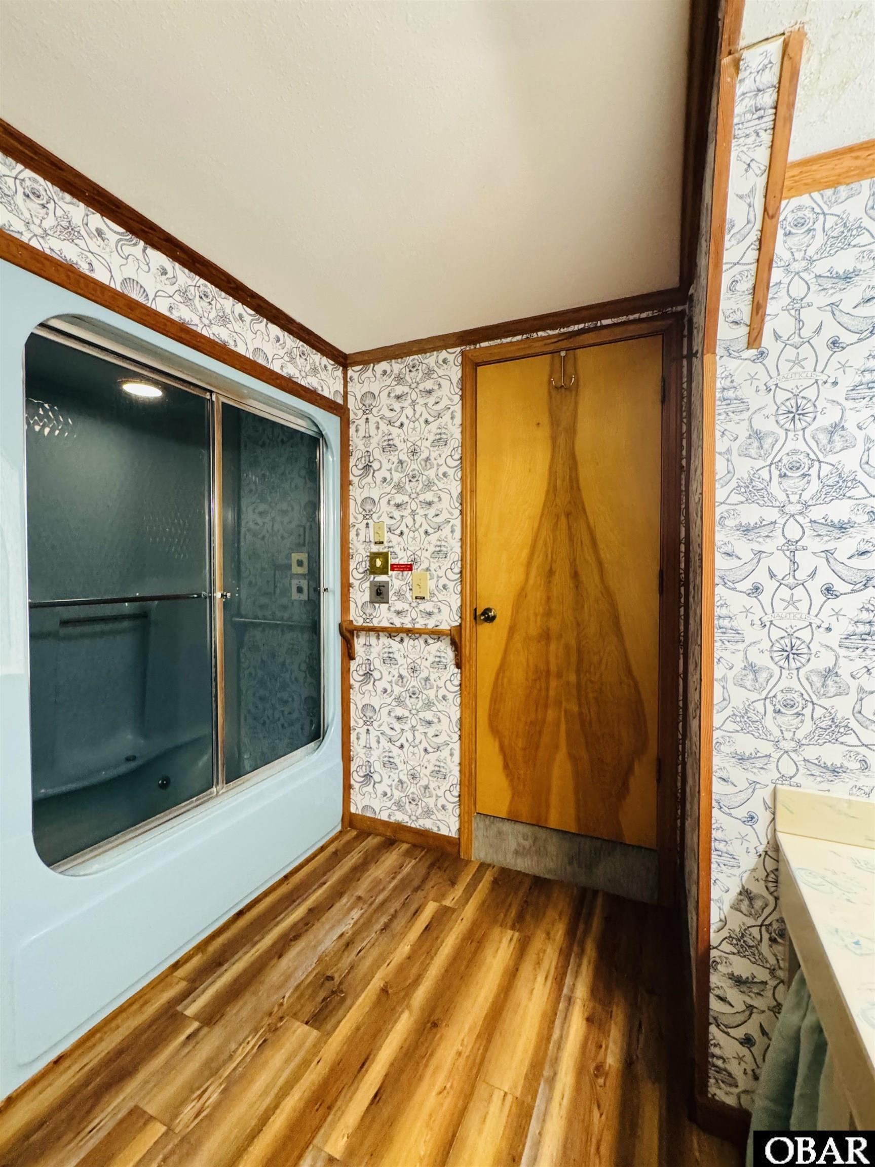 Bathroom with frosted-glass shower, nautical wallpaper, and wood-look flooring.