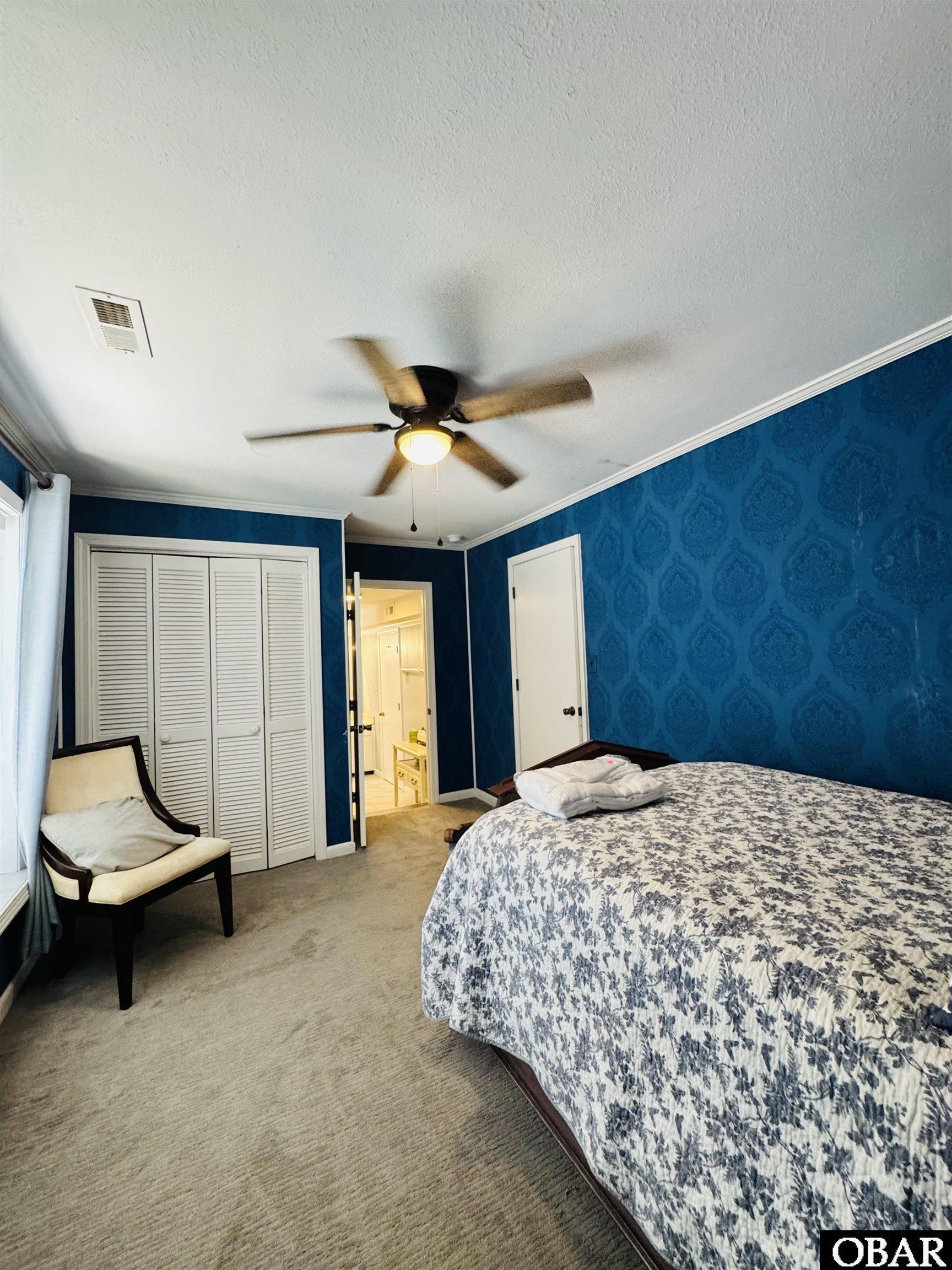 Bedroom with blue patterned walls, floral bedding, louvered closet doors, and a ceiling fan.