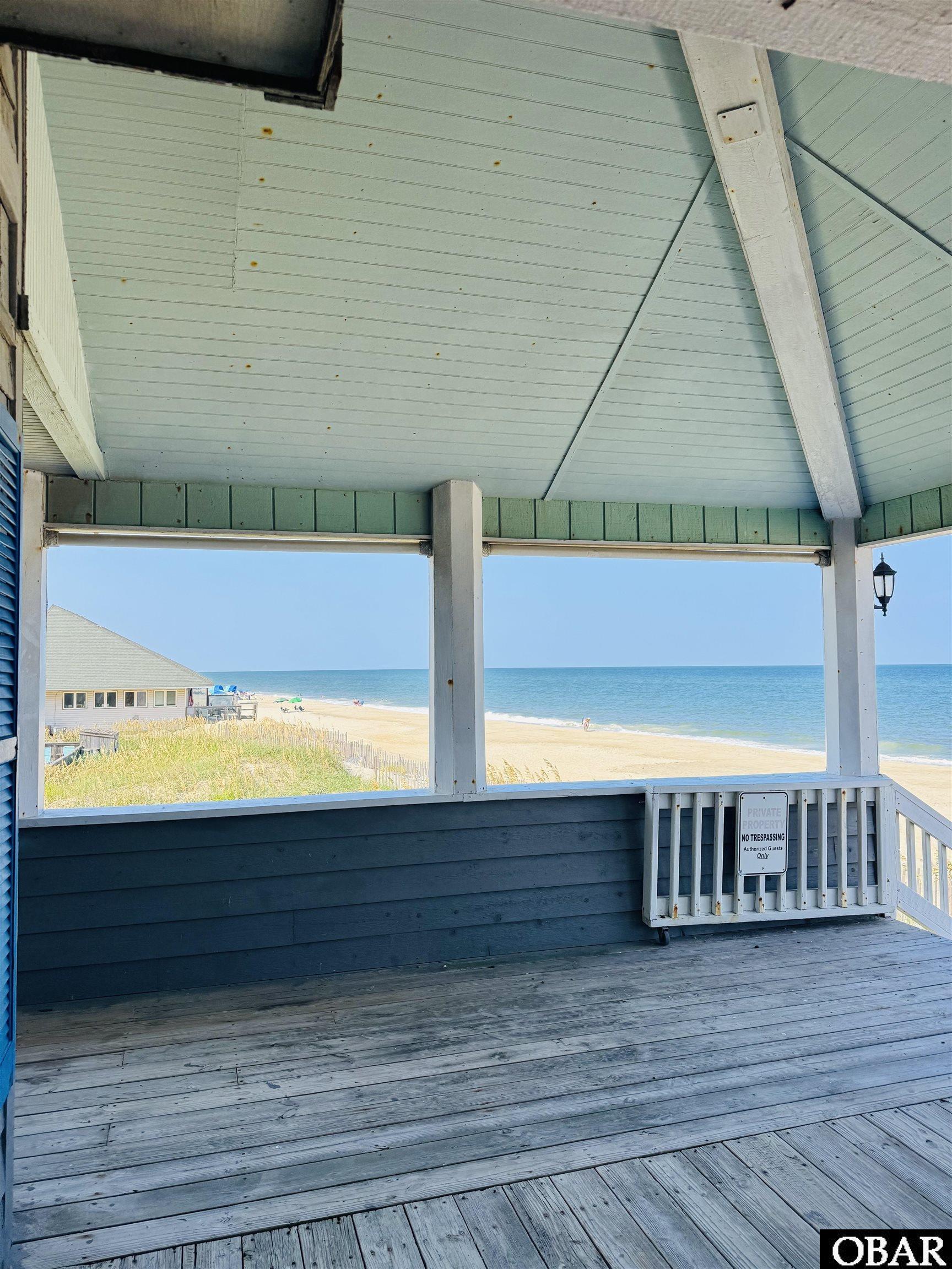 Covered porch overlooking a sandy beach and ocean, with white beams and a private property sign.