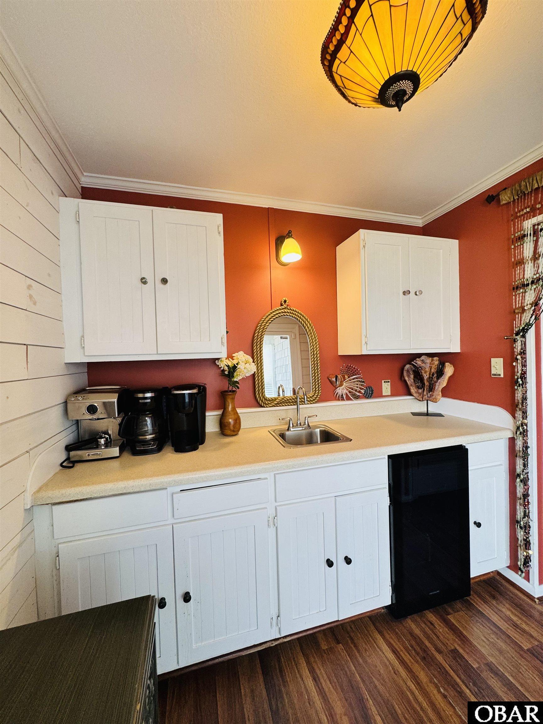 Kitchenette with white cabinets, a sink, red walls, and a black under-counter refrigerator.