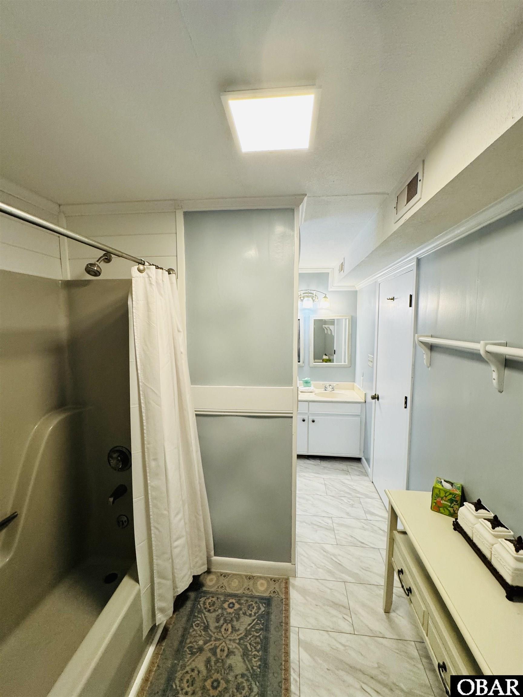 Bathroom with a curtained tub, white vanity, and marble-look floor tiles.
