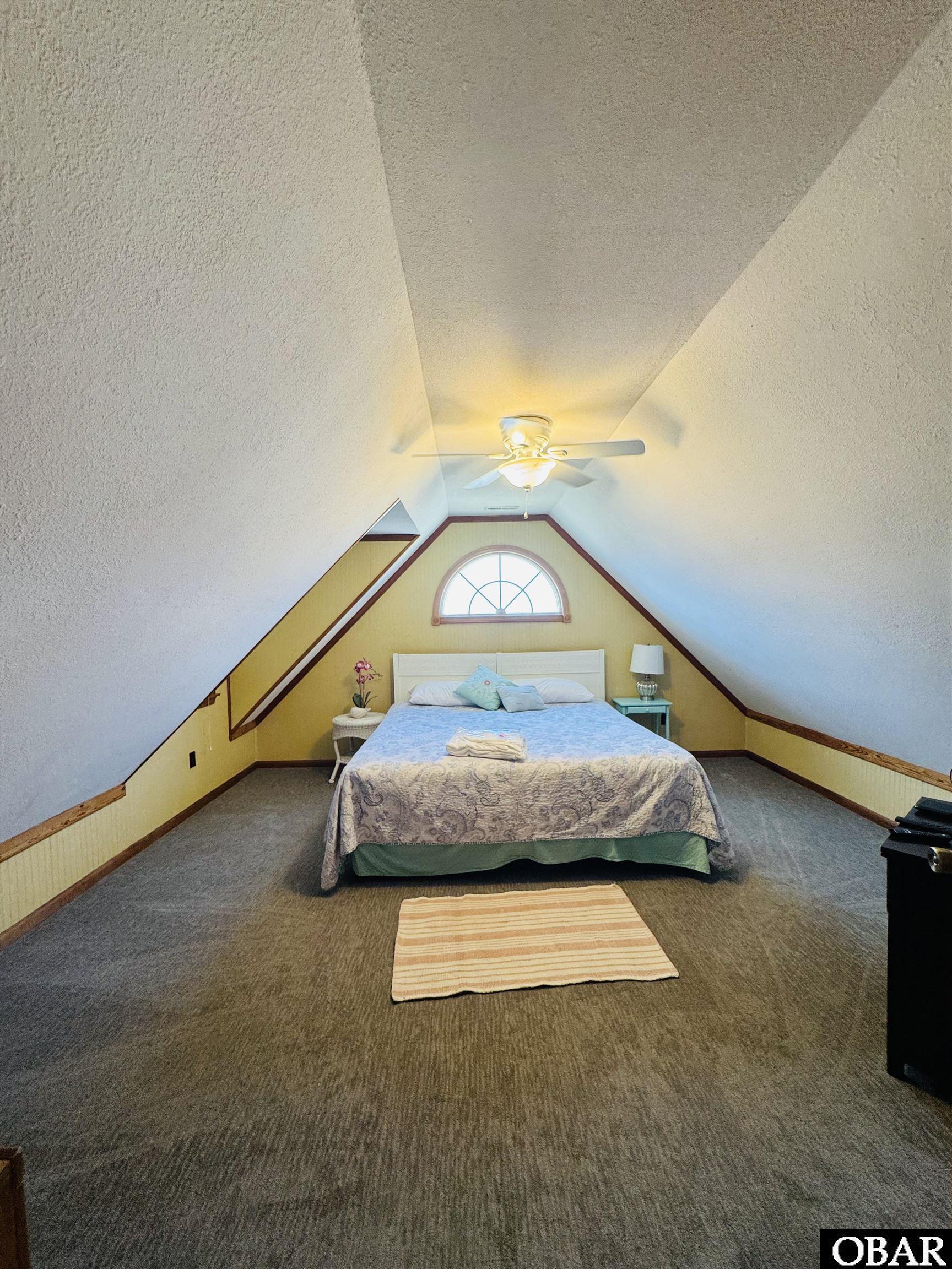 Bedroom with a centered bed beneath a half-moon window and high vaulted ceiling.