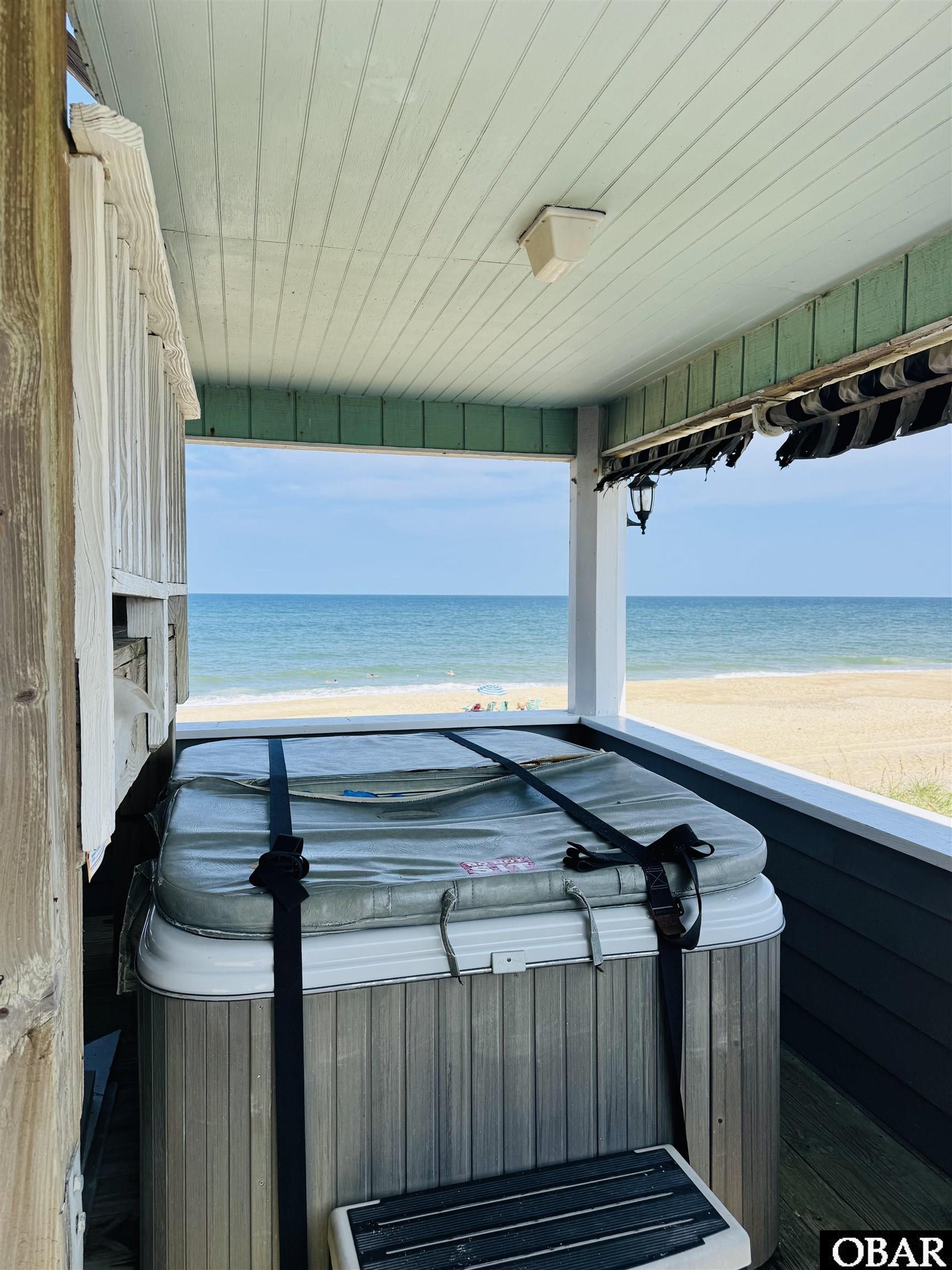Covered deck hot tub overlooking a sandy beach and ocean.
